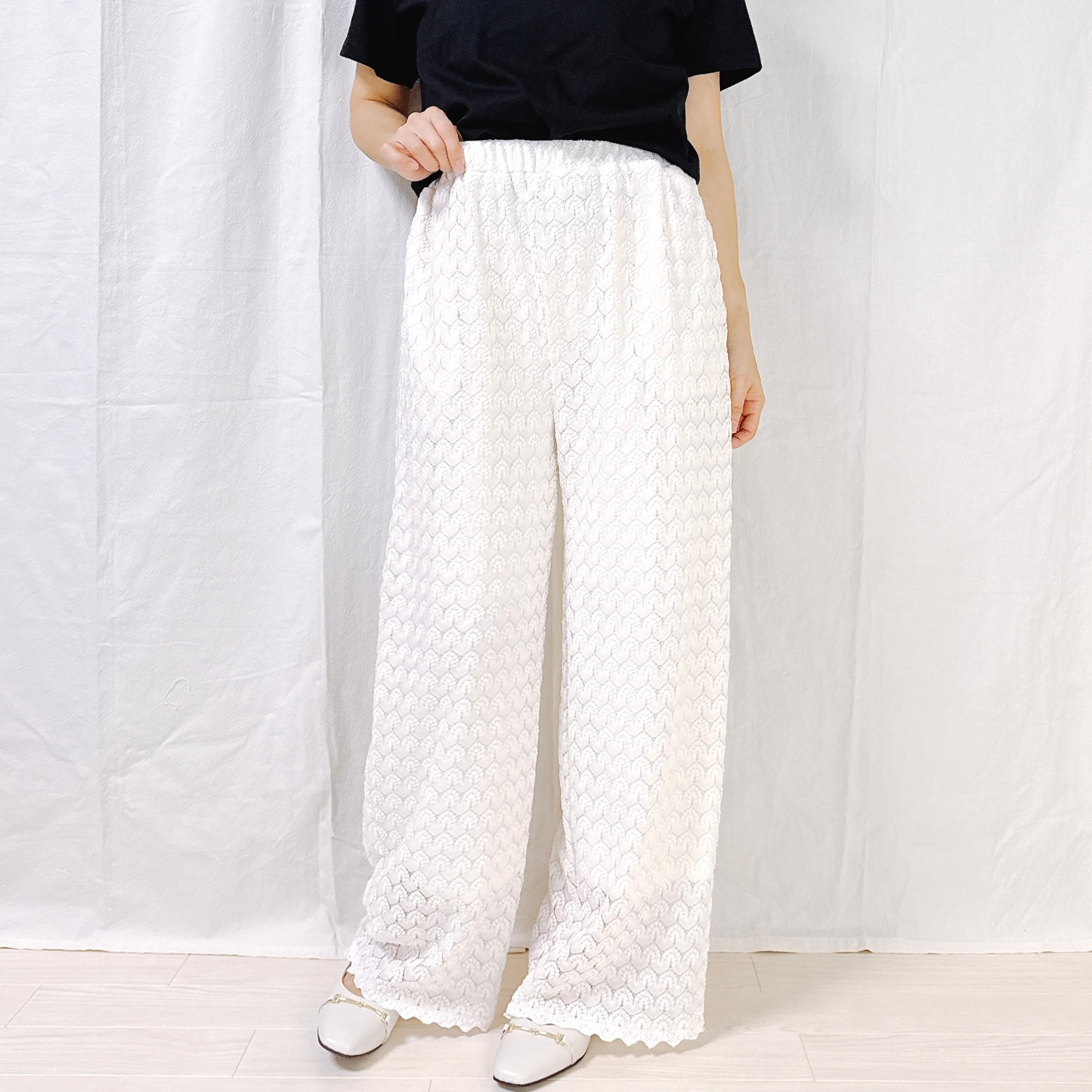 Person wearing a black top and wide-legged patterned pants, standing against a white background