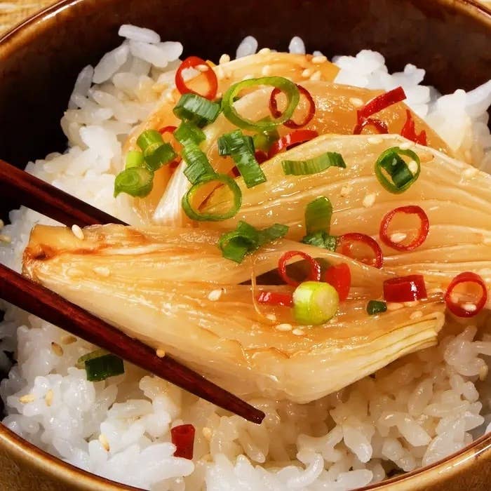 ご飯の上にキムチとネギ、ゴマをトッピングし、箸で持ち上げている様子。