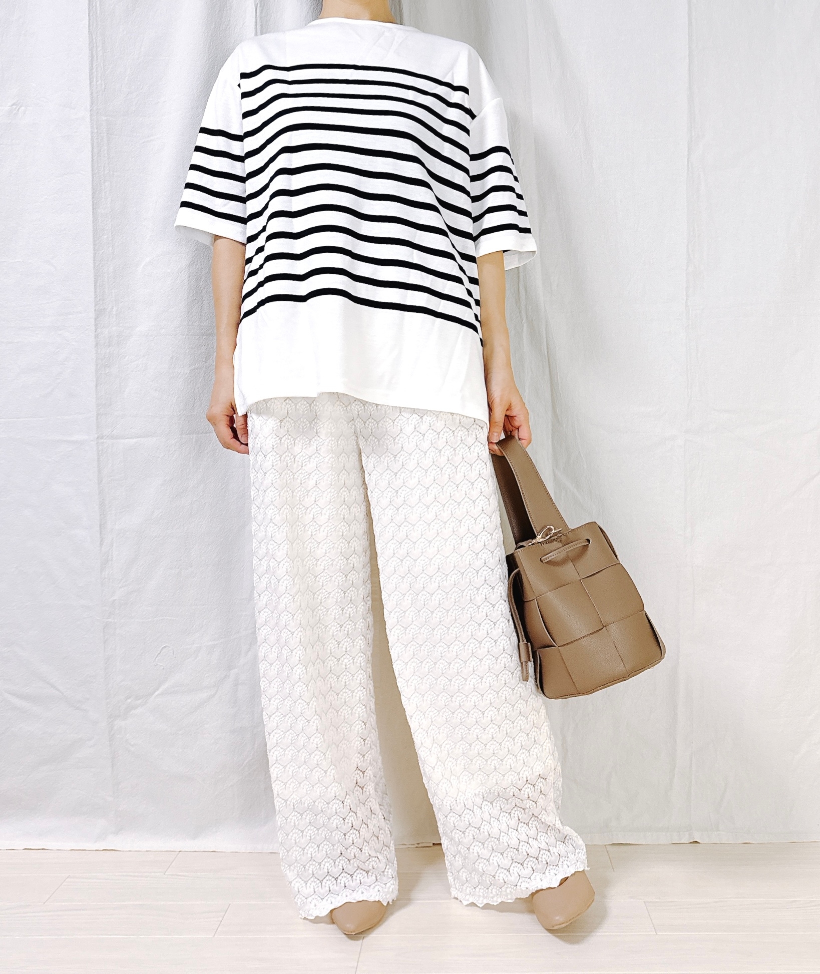 Person stands wearing a loose, striped shirt and patterned wide-leg pants, holding a brown handbag. Face not visible