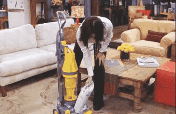 Person in a living room removes a handheld vacuum from its upright base, preparing to clean