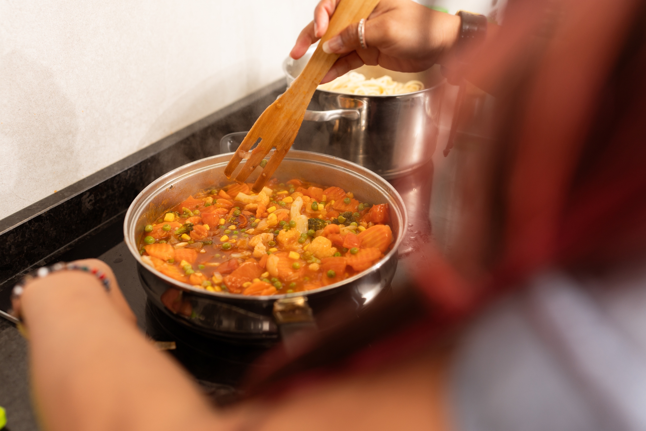Person cooking vegetable stew in a pan on a stovetop, stirring ingredients with a wooden spatula