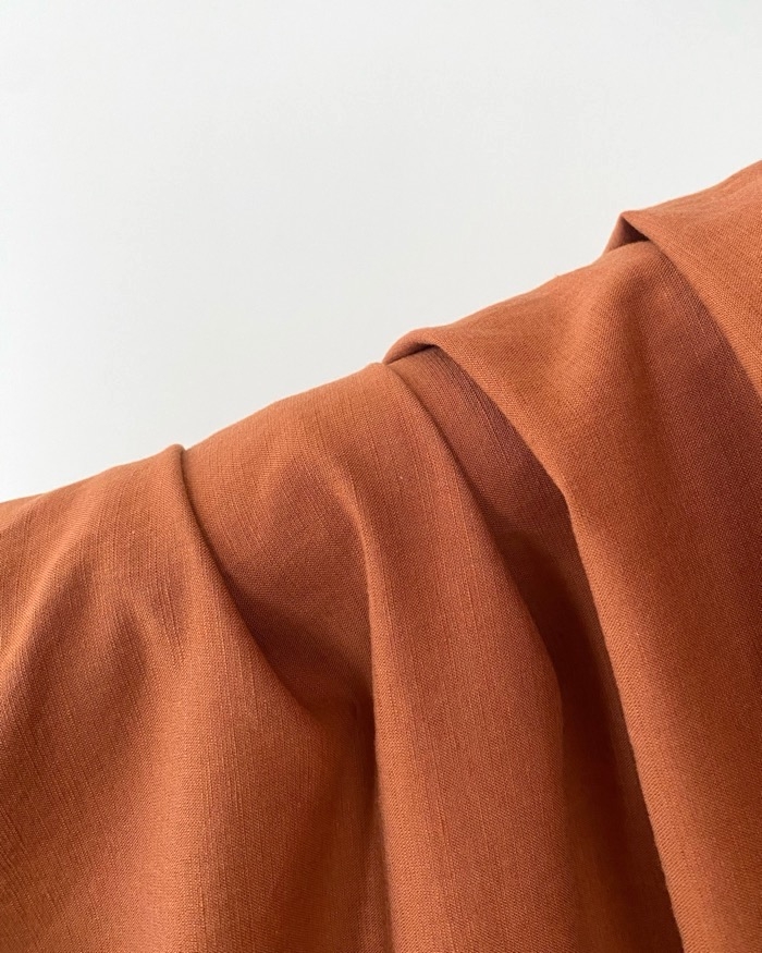 Close-up of rust-colored fabric with folds and draping, creating a sense of texture and softness
