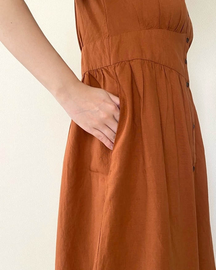 Person in a sleeveless dress with buttons, hand placed casually in a side pocket