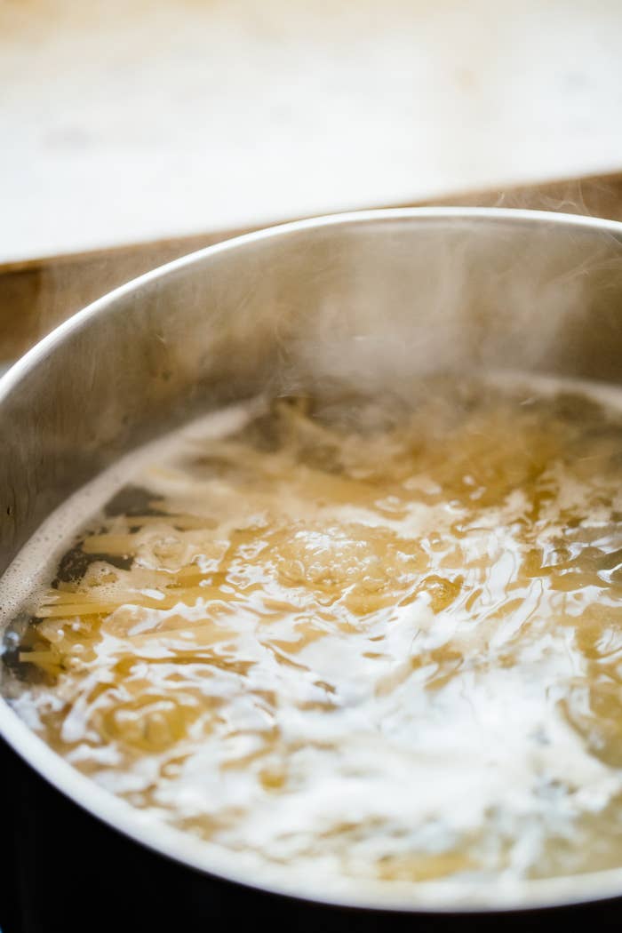 Pot of boiling water with pasta cooking inside, steam rising from the surface