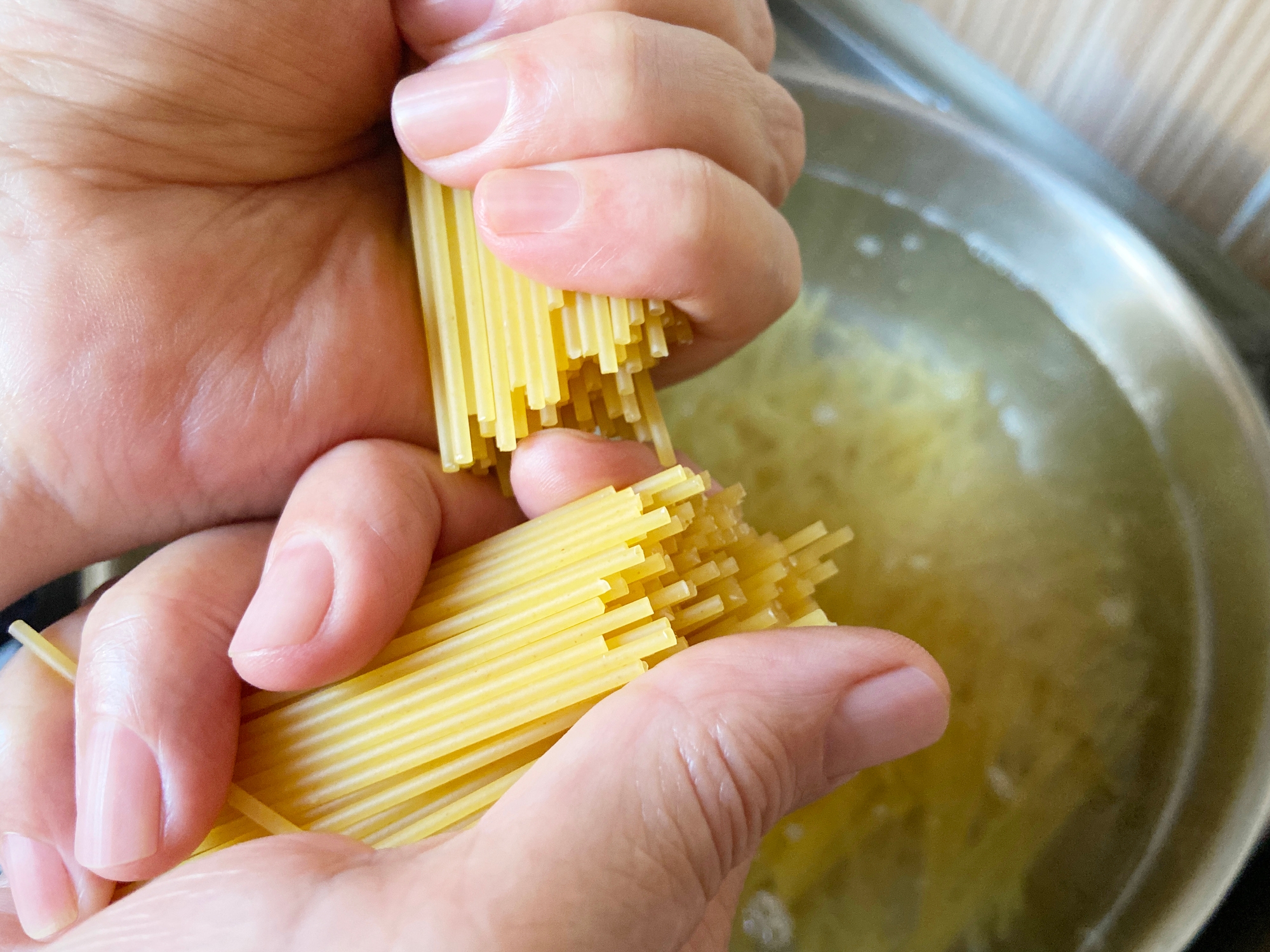 Hands breaking uncooked spaghetti before adding it to a pot of boiling water