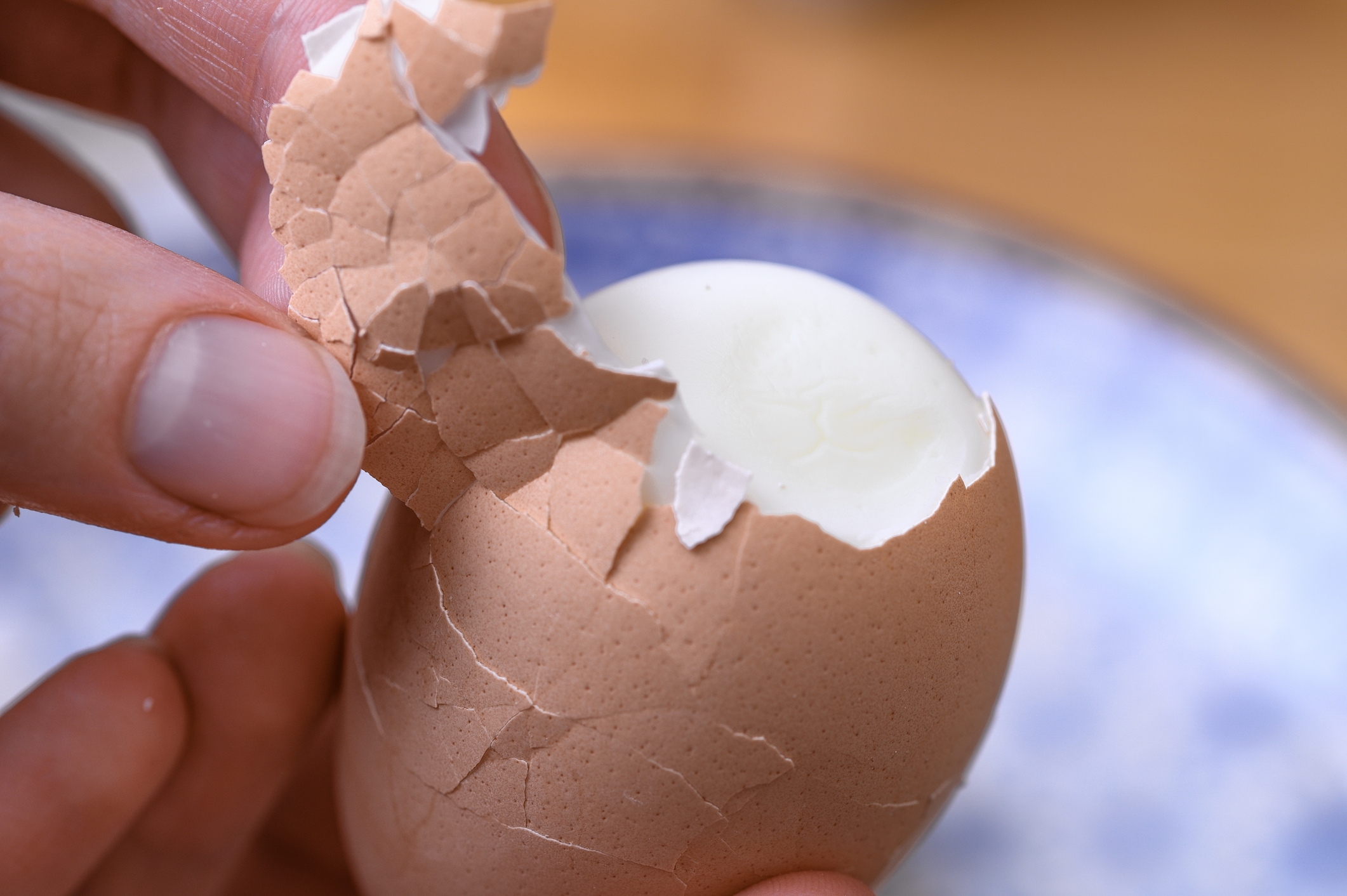Person peeling a hard-boiled egg, removing the cracked shell with fingertips