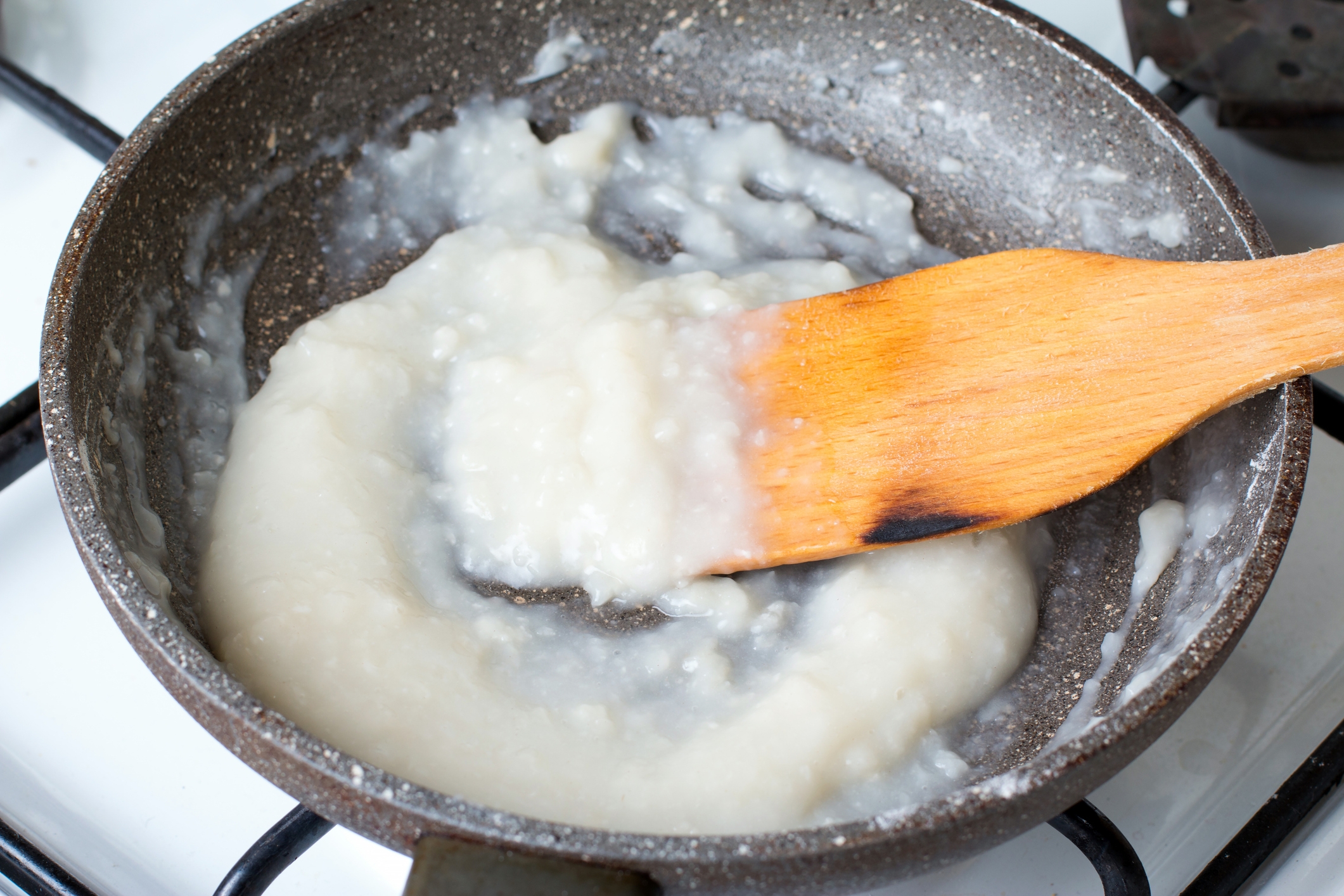 Pan with wooden spatula stirring a thick, white, creamy mixture on a stovetop