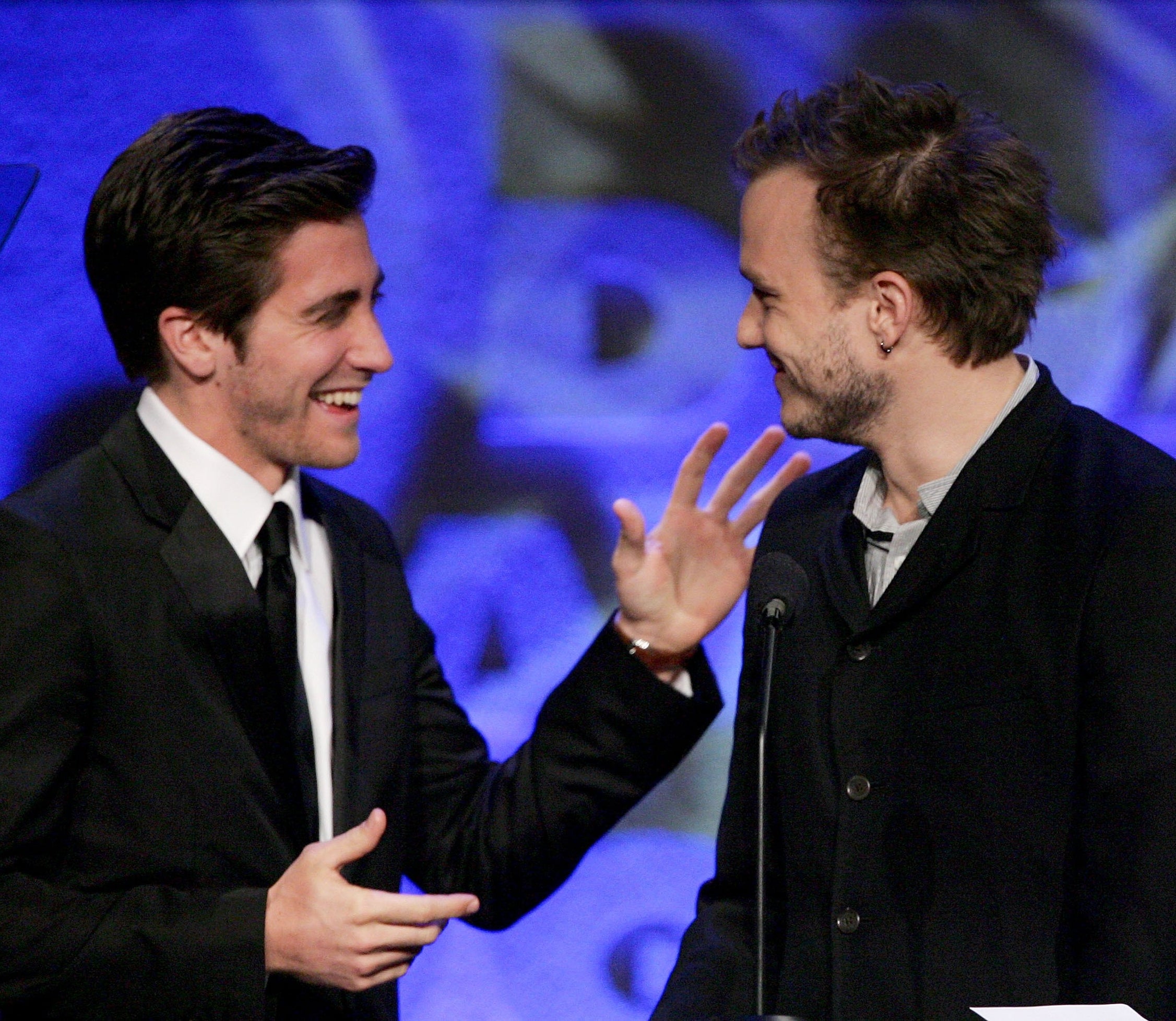 Jake Gyllenhaal and Heath Ledger smiling at each other on stage