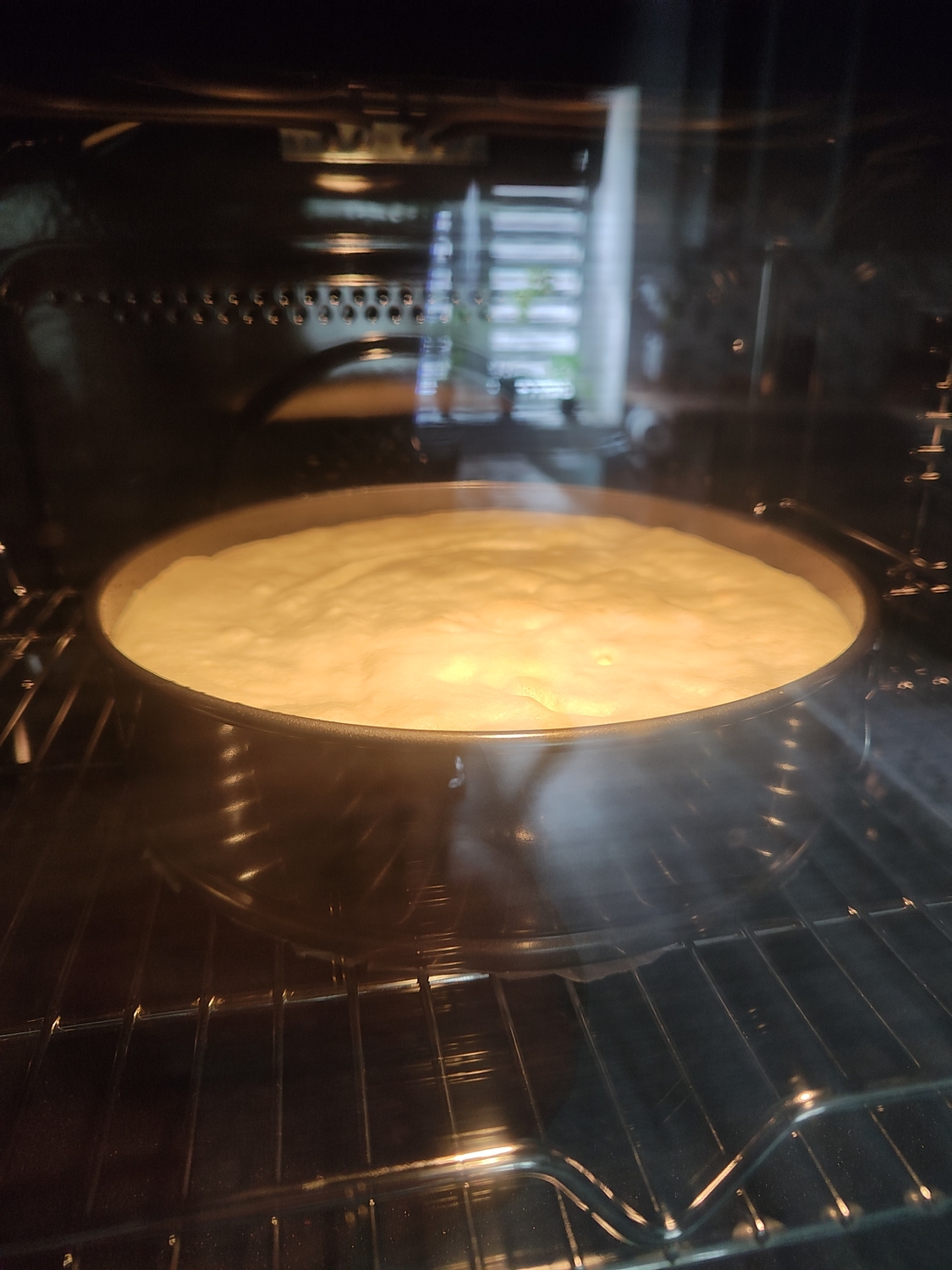 Cake batter in a round pan baking in an oven, visible through the glass door