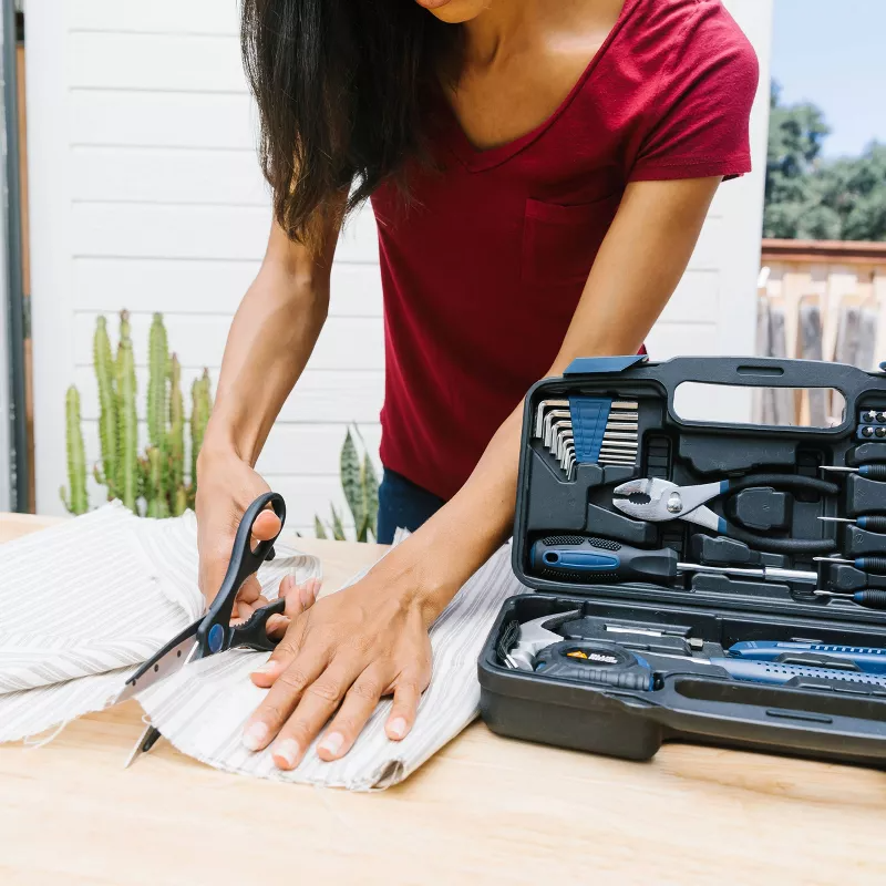 A person in a red shirt cuts fabric with scissors next to an open toolkit