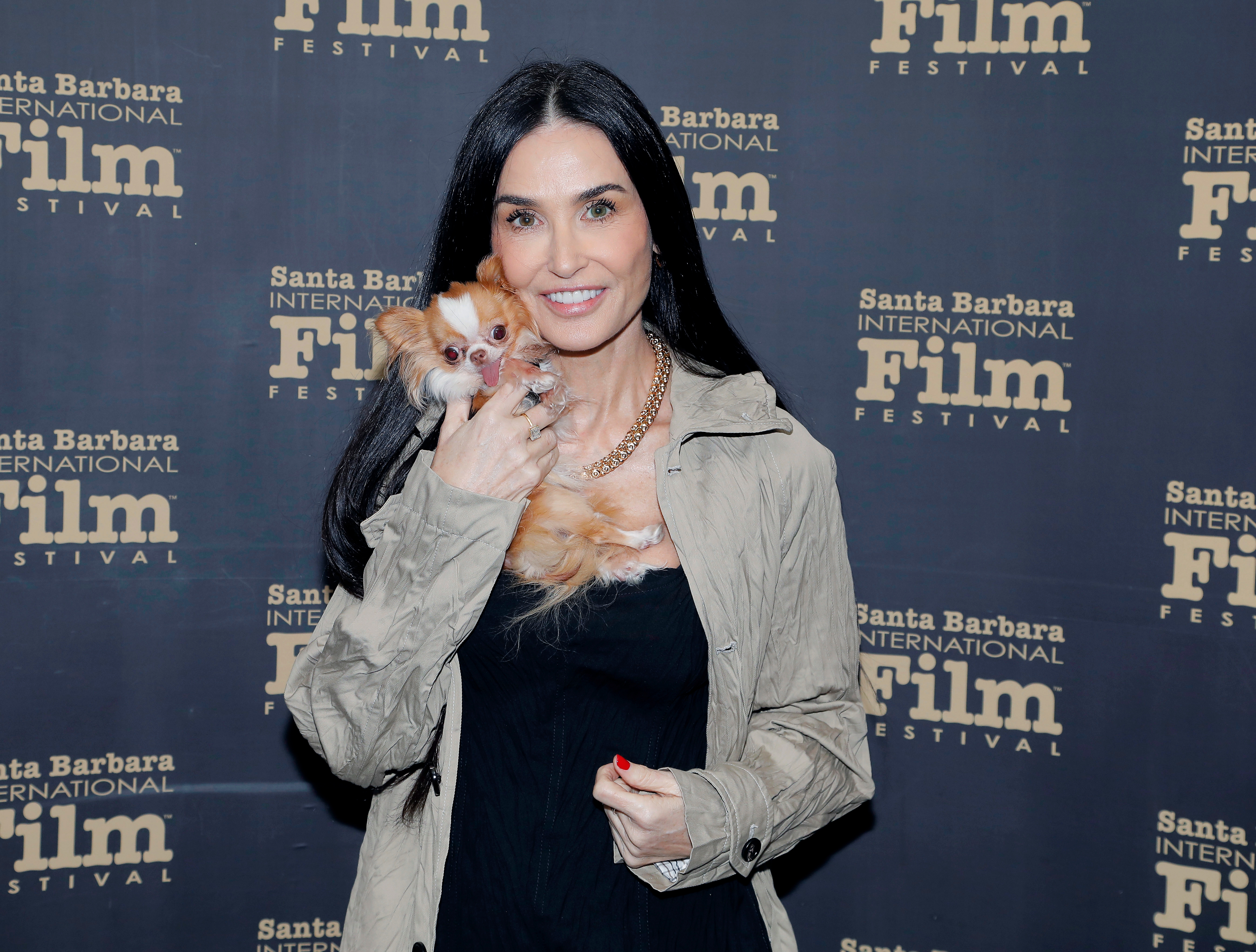 Person holding a small dog at the Santa Barbara International Film Festival, wearing a casual jacket over a black top