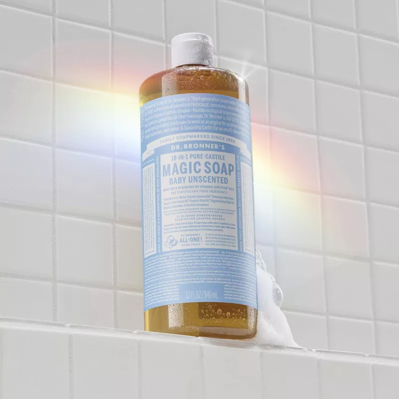 A bottle of Dr. Bronner's 18-in-1 Magic Soap sits on a tiled shower ledge, featuring a label with product information