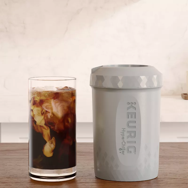 Iced coffee in a glass next to a Keurig HyperChiller on a wooden table, used to quickly chill drinks
