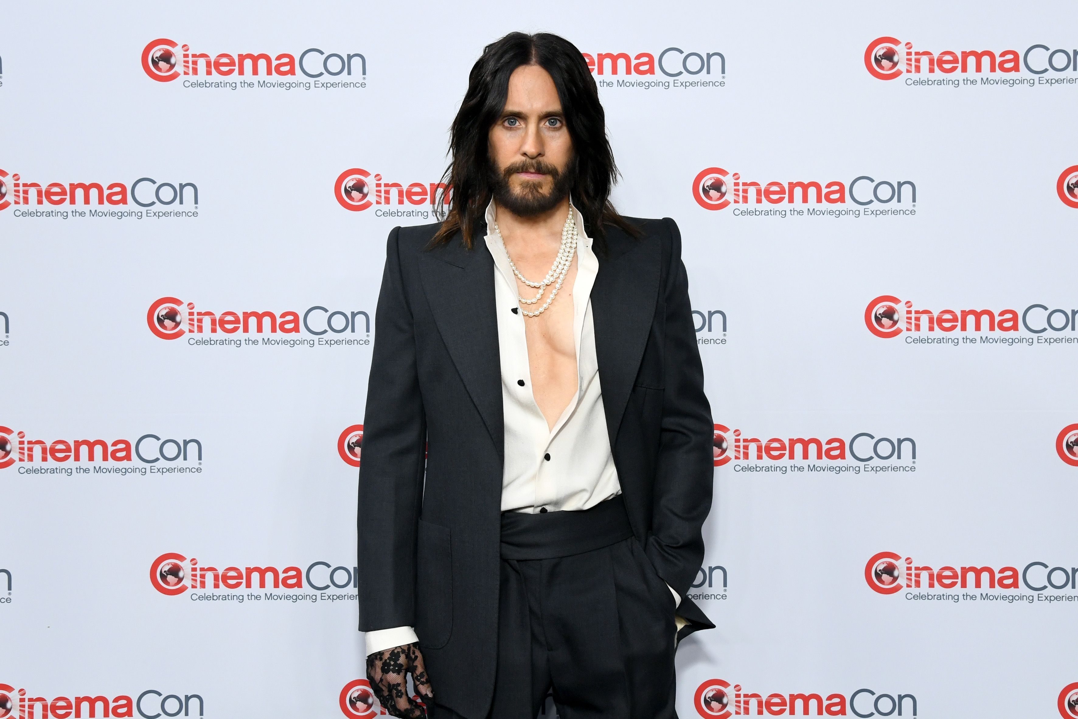 Person on red carpet in elegant black suit with deep V neckline and pearl necklace, at CinemaCon event backdrop