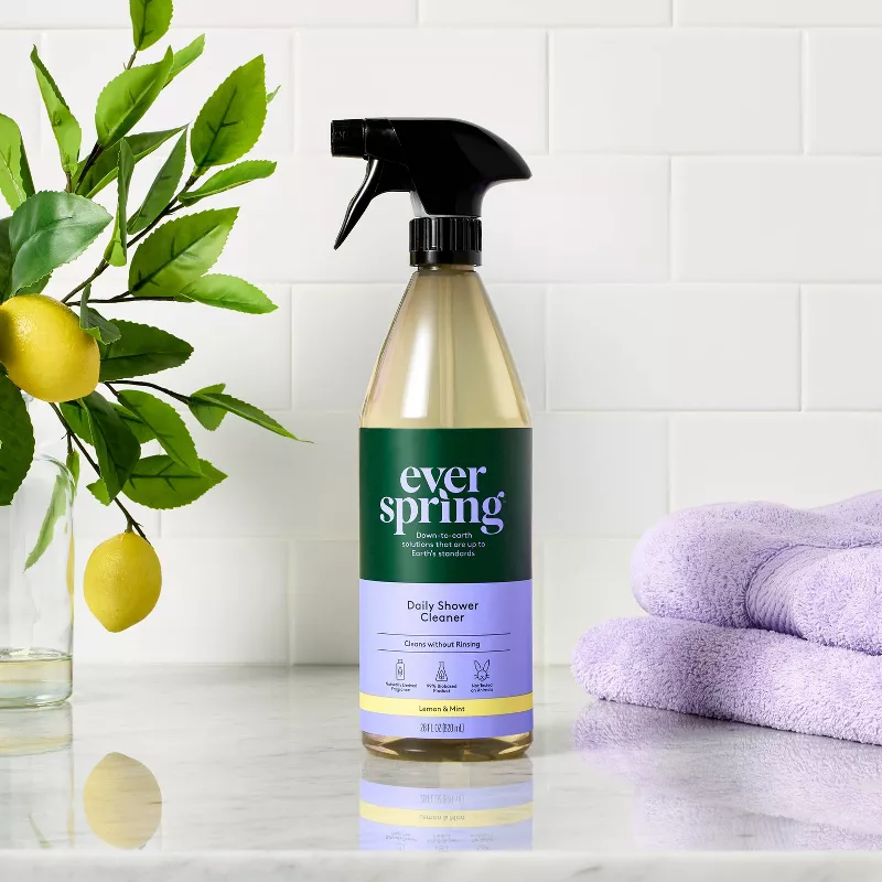 Spray bottle of Everspring Daily Shower Cleaner on a white tile counter beside lemons and folded towels