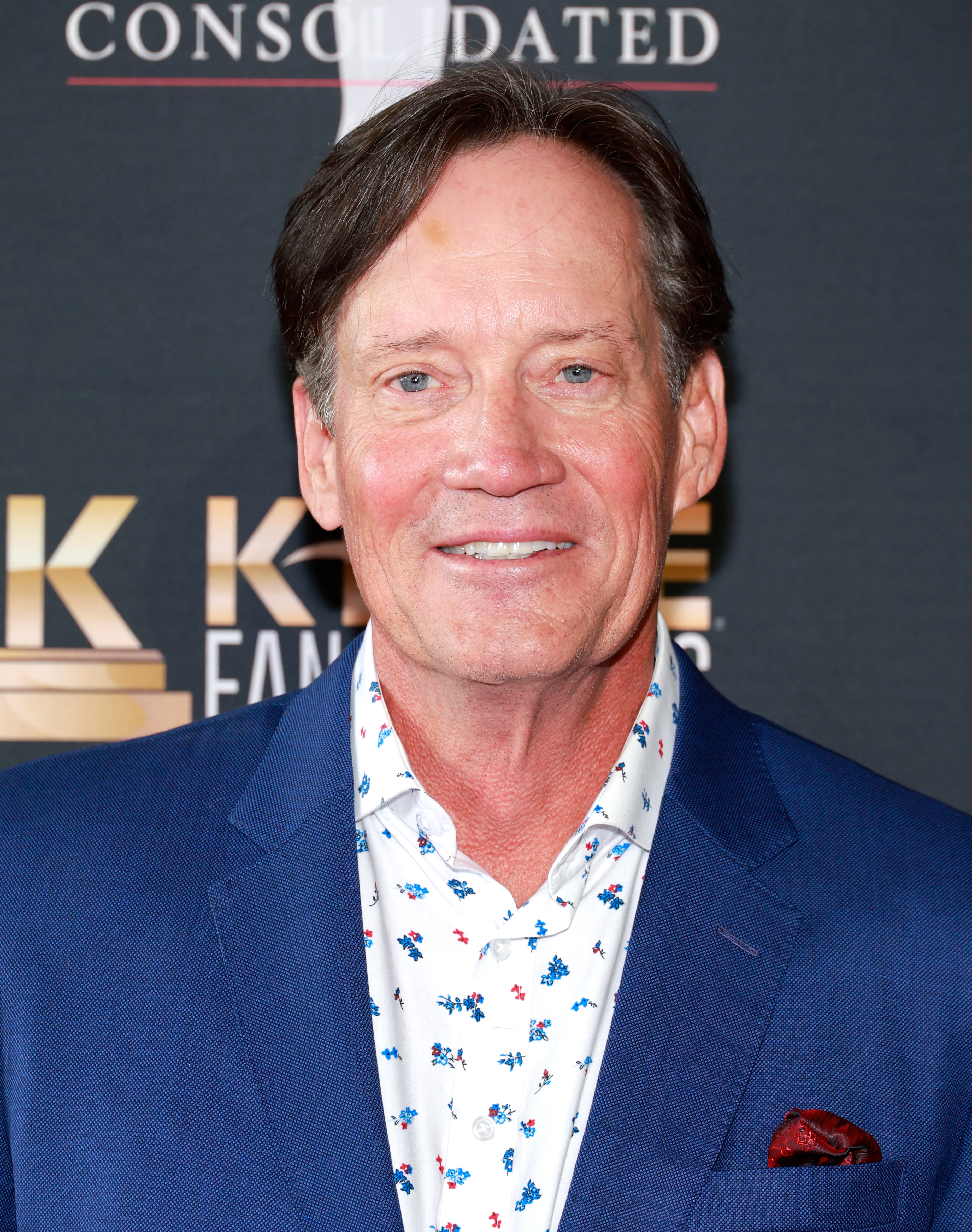 A person wearing a blue suit and a patterned shirt smiles at a formal event