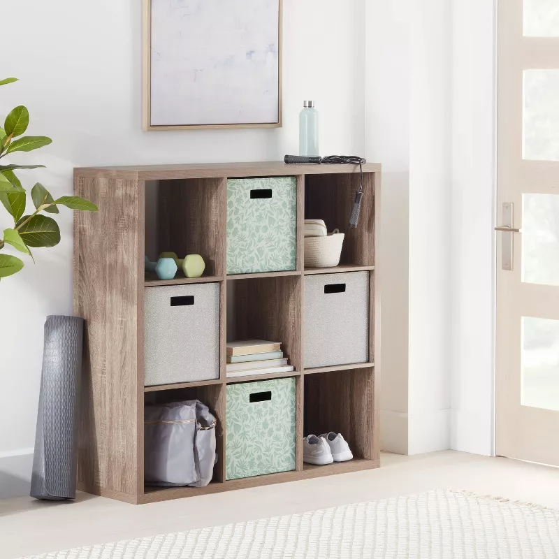 Wooden storage unit with nine cubbies, featuring bins, decorative items, and a rolled yoga mat nearby, perfect for organized home storage