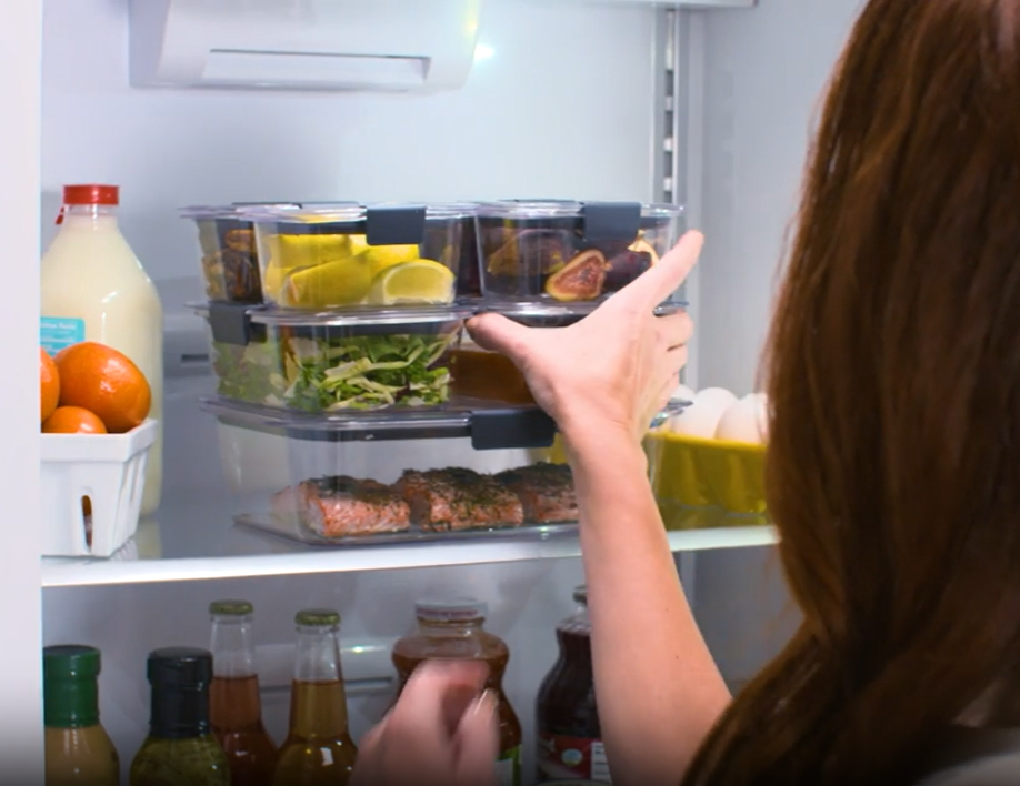 Person organizing food containers in a fridge with visible milk, eggs, and condiments