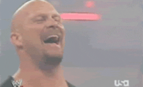Man laughing heartily in a wrestling ring, wearing a sleeveless top