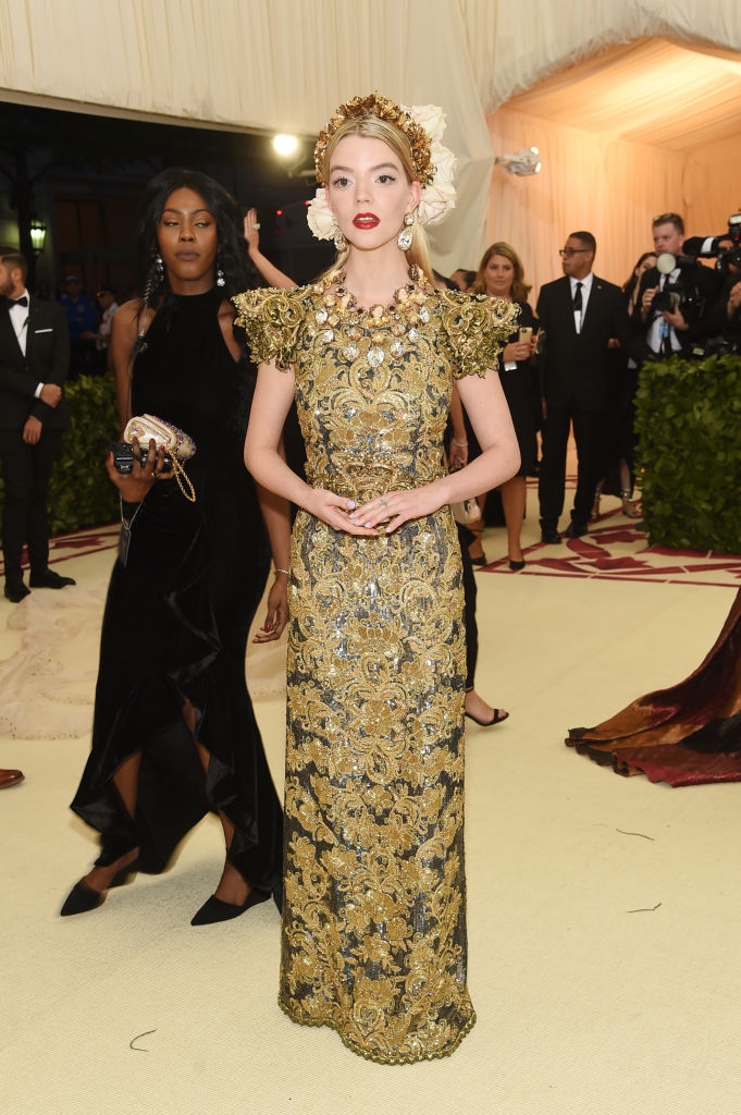 Anya wearing an ornate, floral-patterned gown with elaborate shoulder details and a headpiece adorned with flowers