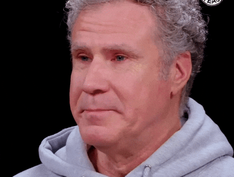 Person in a gray hoodie reacting with a slight smile and head nod, sitting against a black background