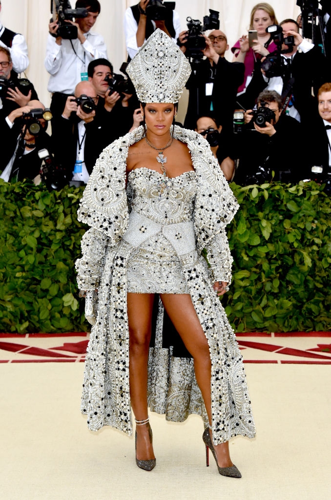 A person in an ornate, embellished outfit, including minidress, coat, and headpiece, resembling papal attire