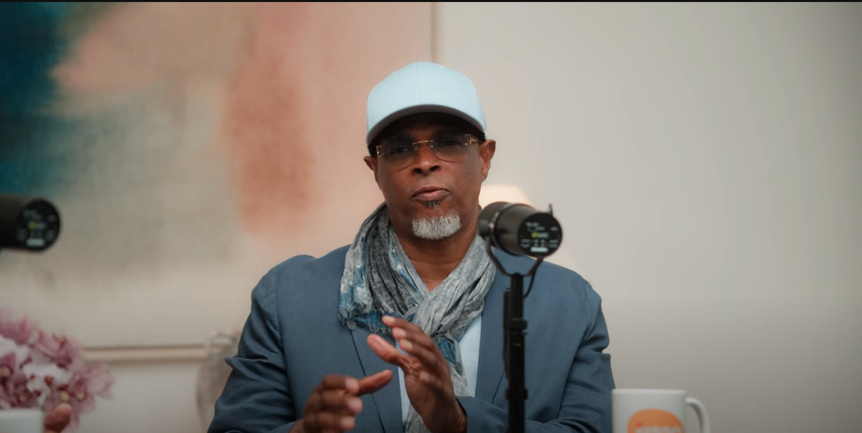 Person in a casual jacket and scarf speaks into a microphone, possibly during a podcast or interview setting