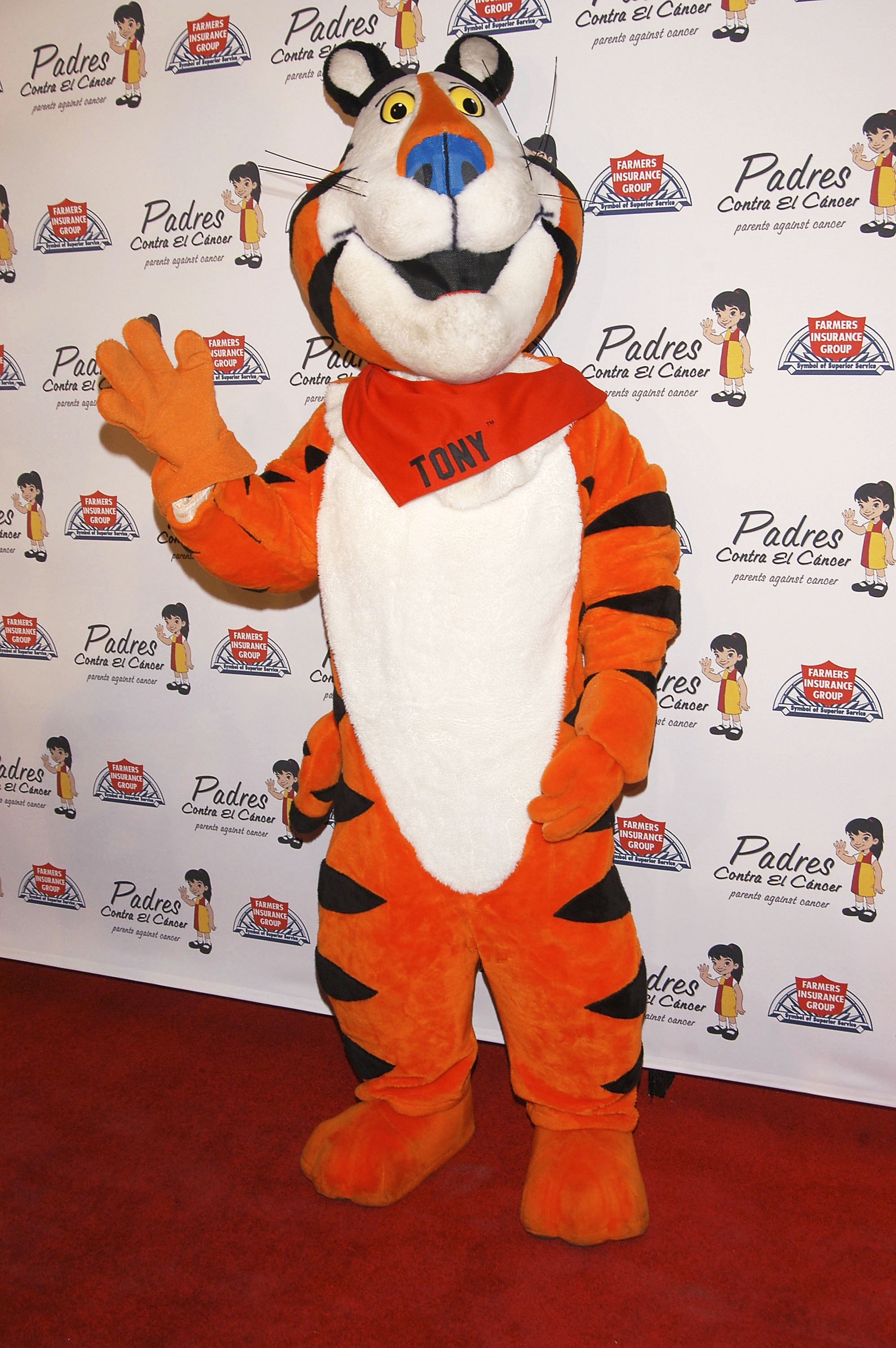 Tony the Tiger mascot waves on a red carpet at a celebrity event, wearing a bandana with "TONY" written on it