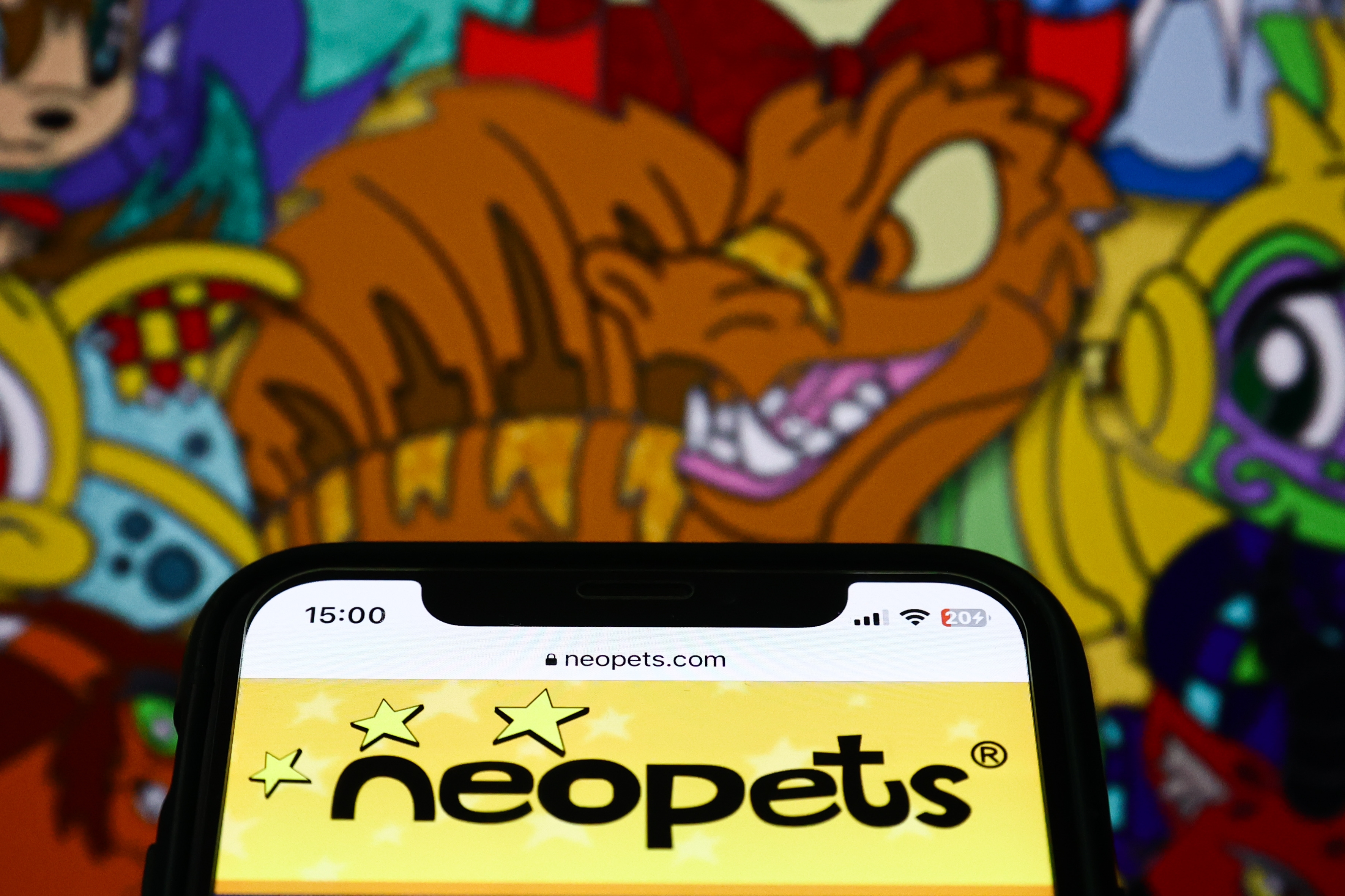 Smartphone showing Neopets website with colorful cartoon characters on screen behind it