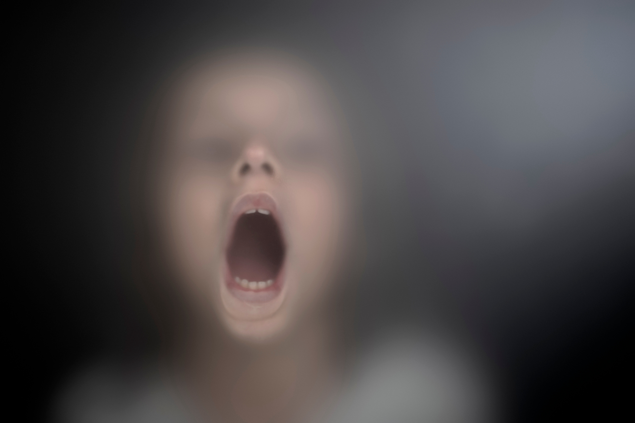 Child with mouth open, blurred background creates a mysterious effect. Image conveys emotion and curiosity, suitable for parenting-related content