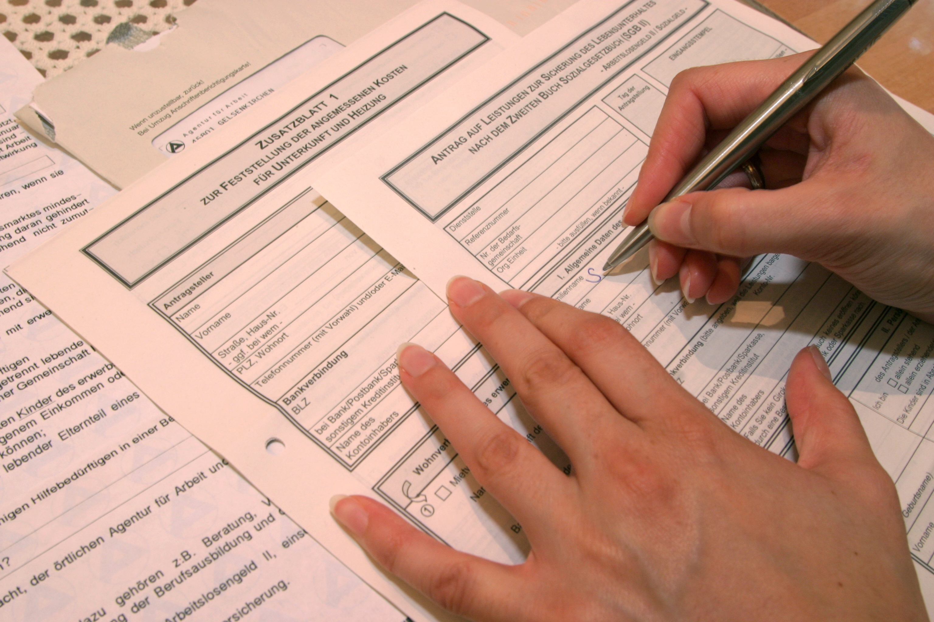 Hands filling out official forms with a pen. Multiple documents are scattered underneath