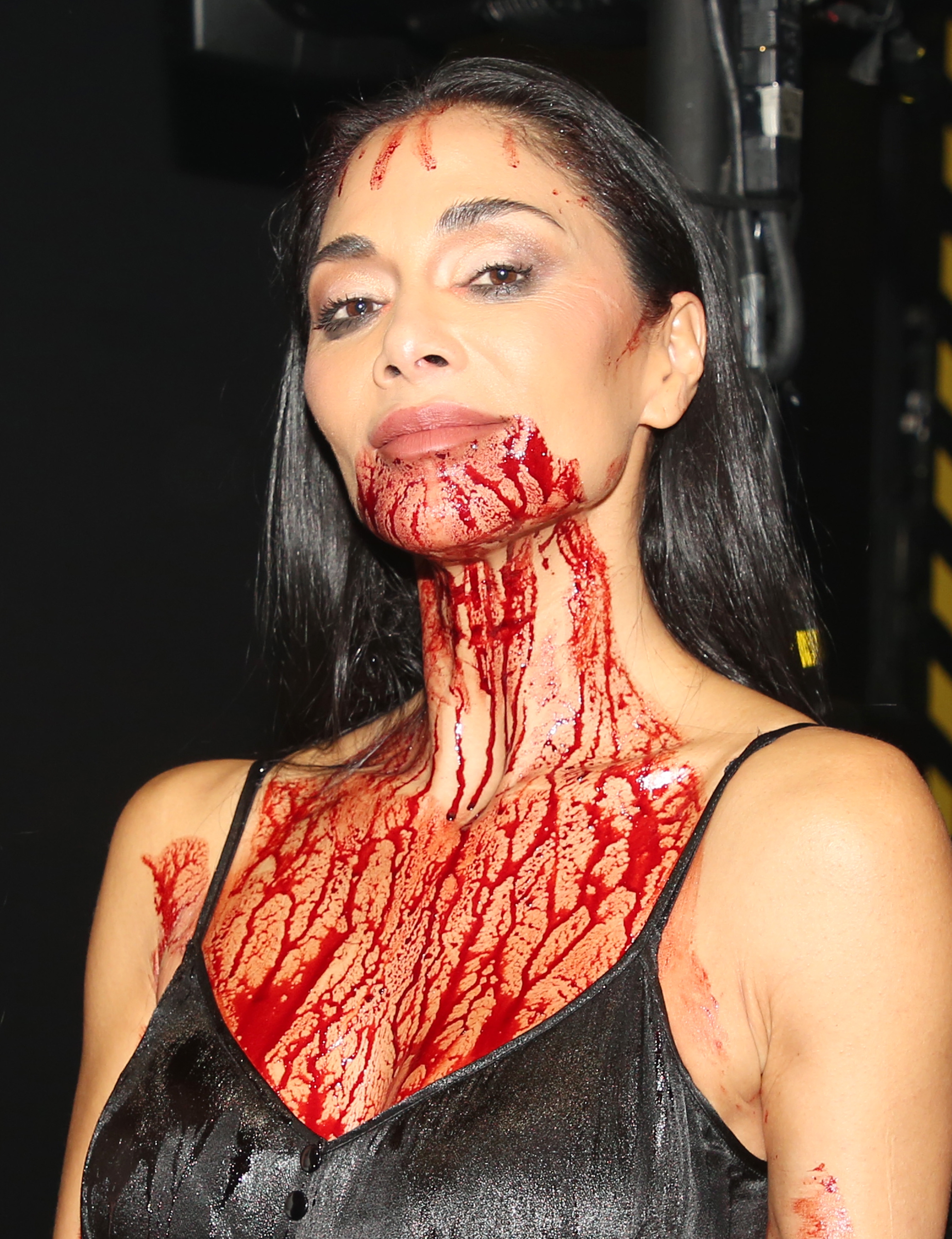 A person in a sleeveless outfit is covered in red liquid, possibly for an effect. They look confidently into the camera