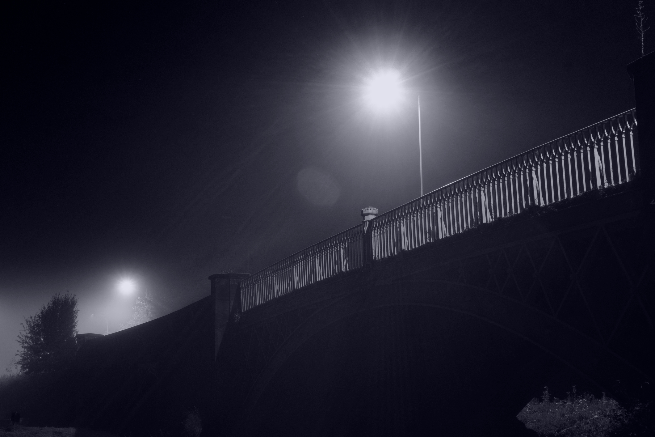 A dimly lit bridge at night with streetlights illuminating the scene, creating a peaceful yet eerie atmosphere