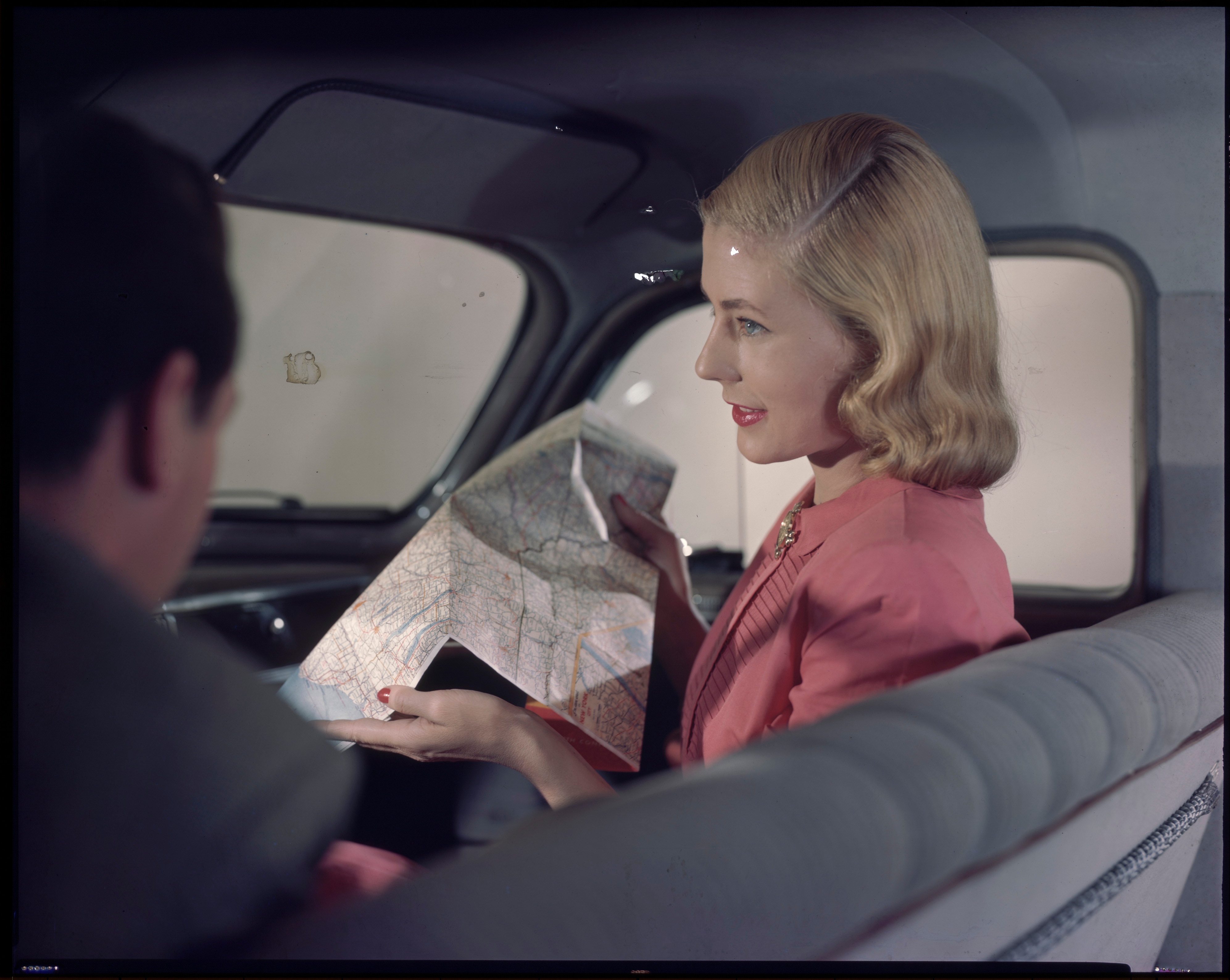 Person in vintage car looking at a map, wearing elegant retro-style clothing, with classic hairstyle
