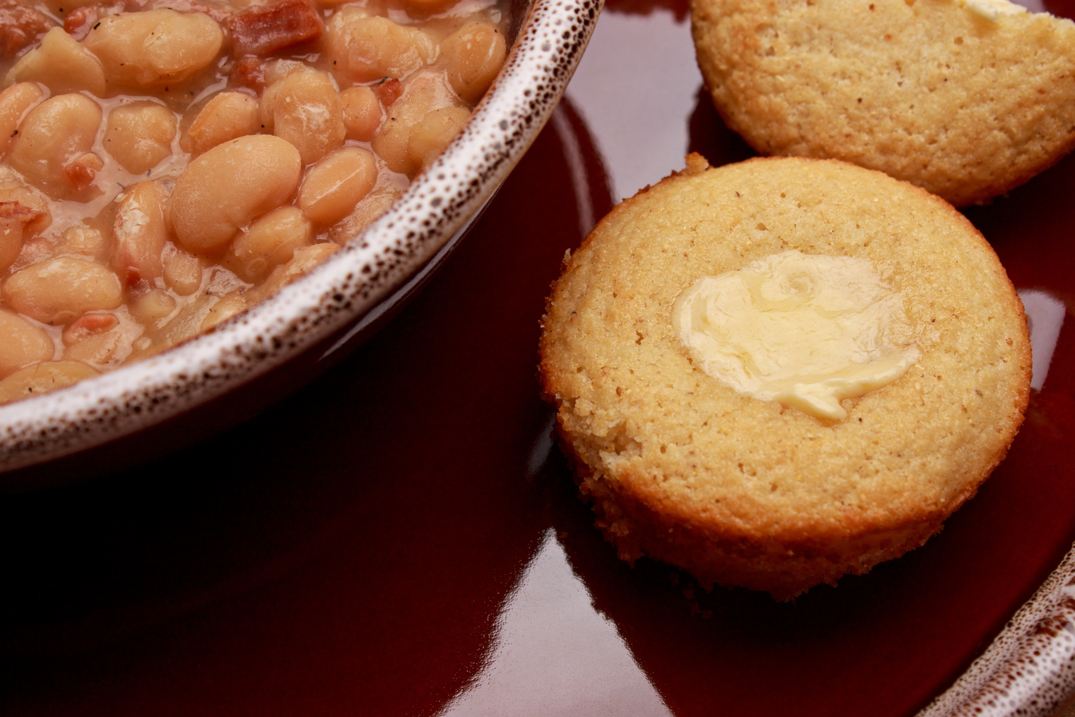 A bowl of bean soup next to a buttered cornbread muffin on a plate