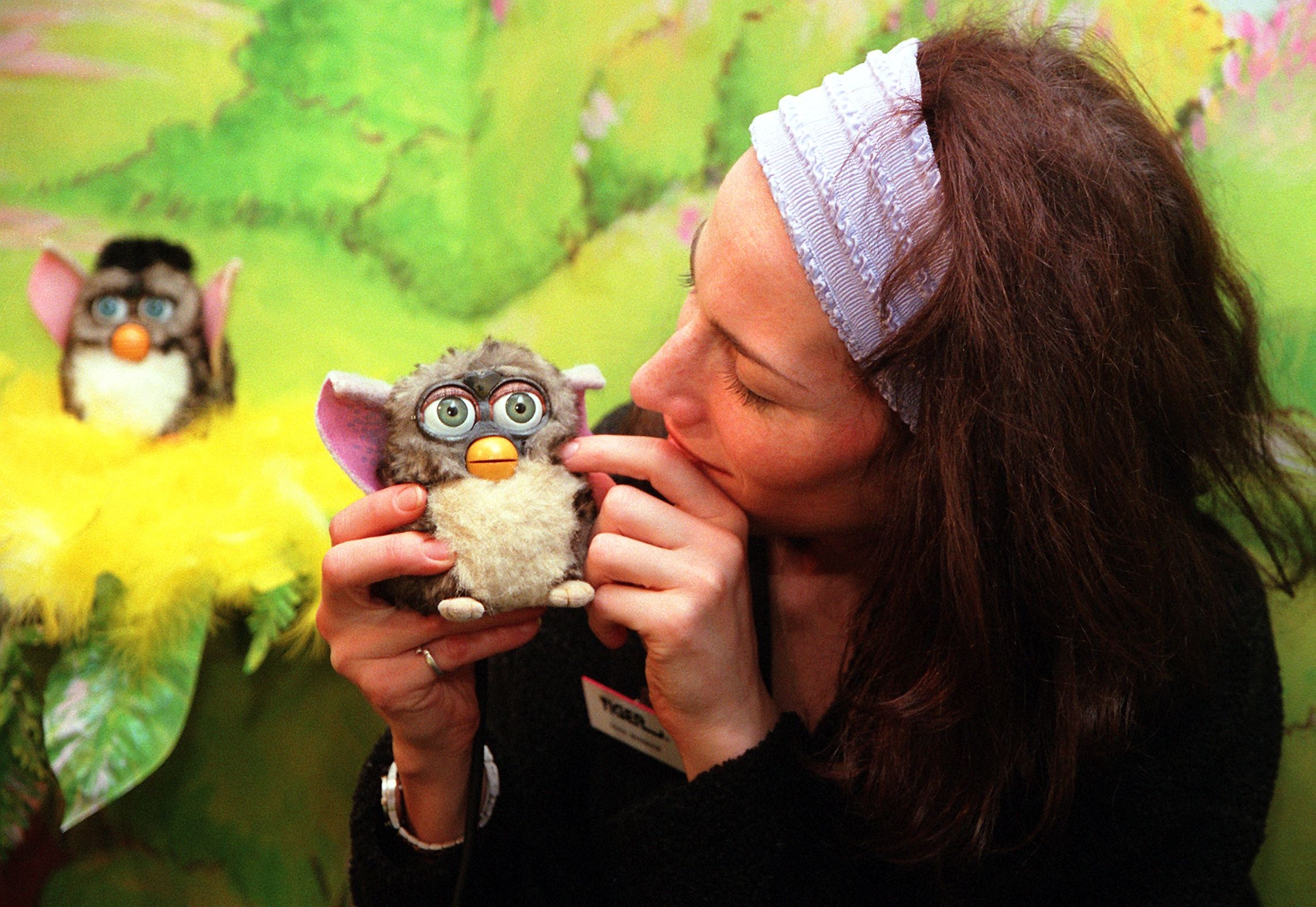 A person holding and playfully interacting with a Furby toy, with another Furby visible in the background nest