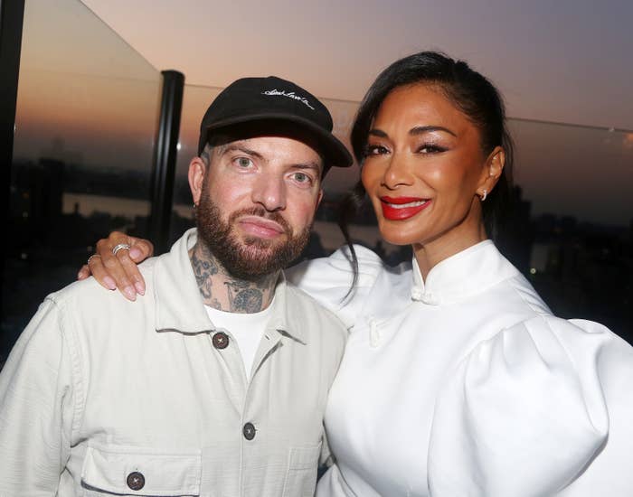 Two individuals posing together outdoors at sunset. The woman is in elegant attire and the man is in casual clothing with a cap