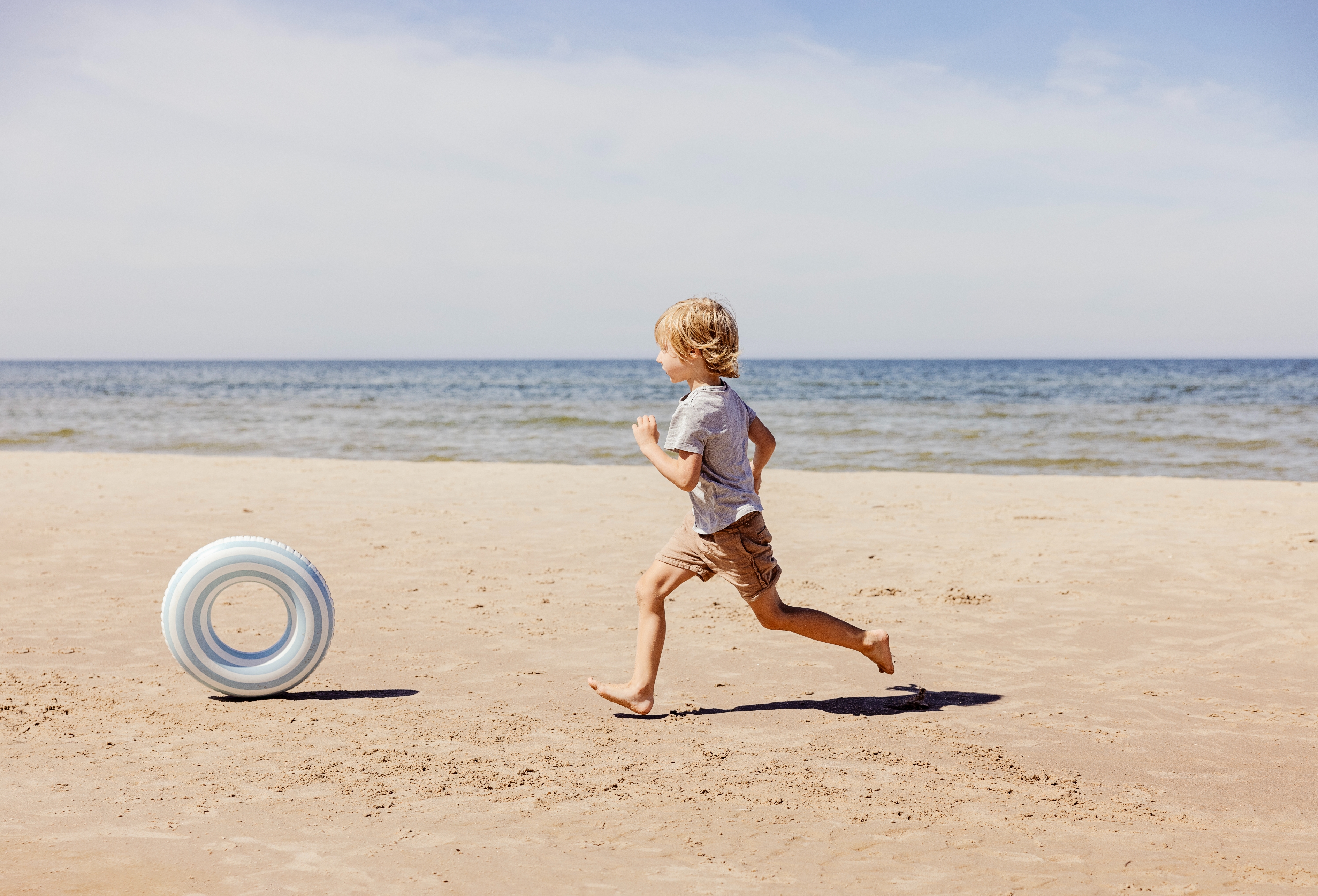 Child running joyfully on a sandy beach near the ocean, chasing a white round object