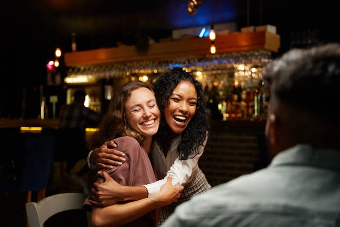 Two friends joyfully hug in a cozy bar setting, creating a warm and cheerful atmosphere