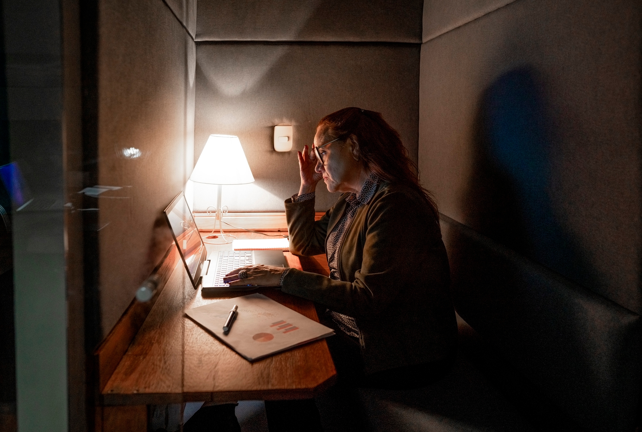 Person in an office booth working on a laptop, adjusts glasses with one hand