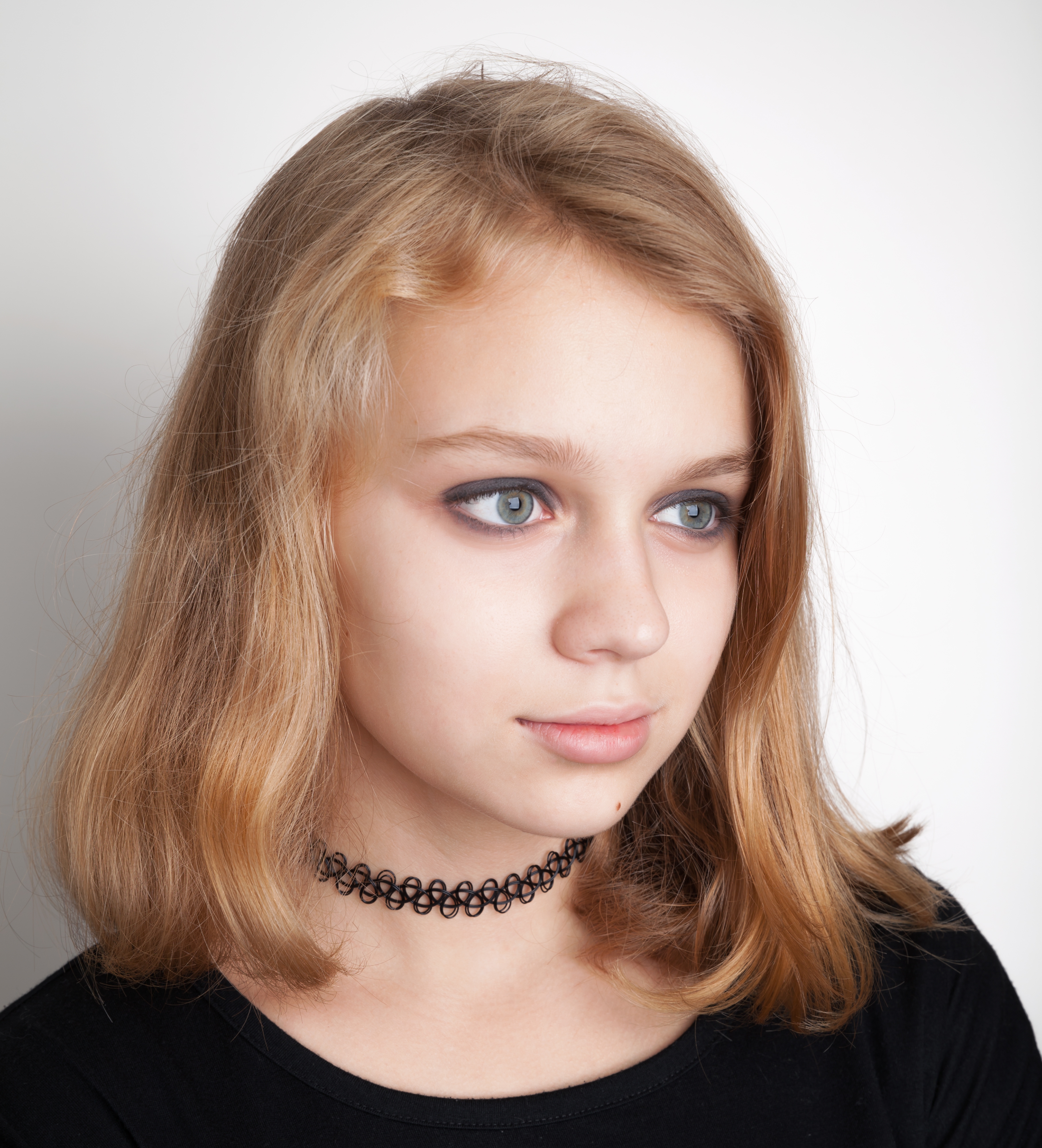 Girl with medium-length hair, wearing a black choker and a black top, looking to the side with a thoughtful expression