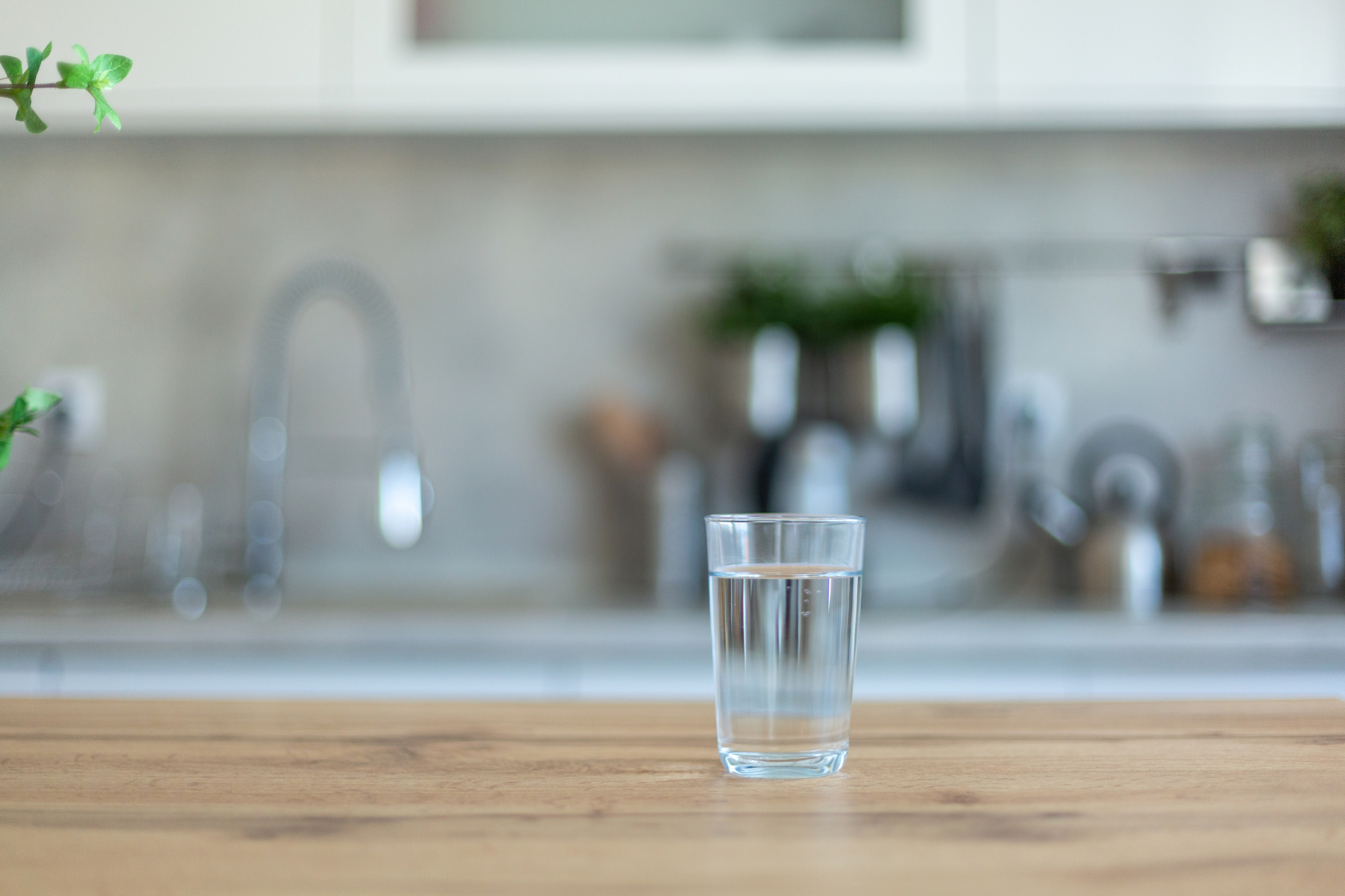 A glass of water on a wooden kitchen counter with a blurred background of kitchen fixtures