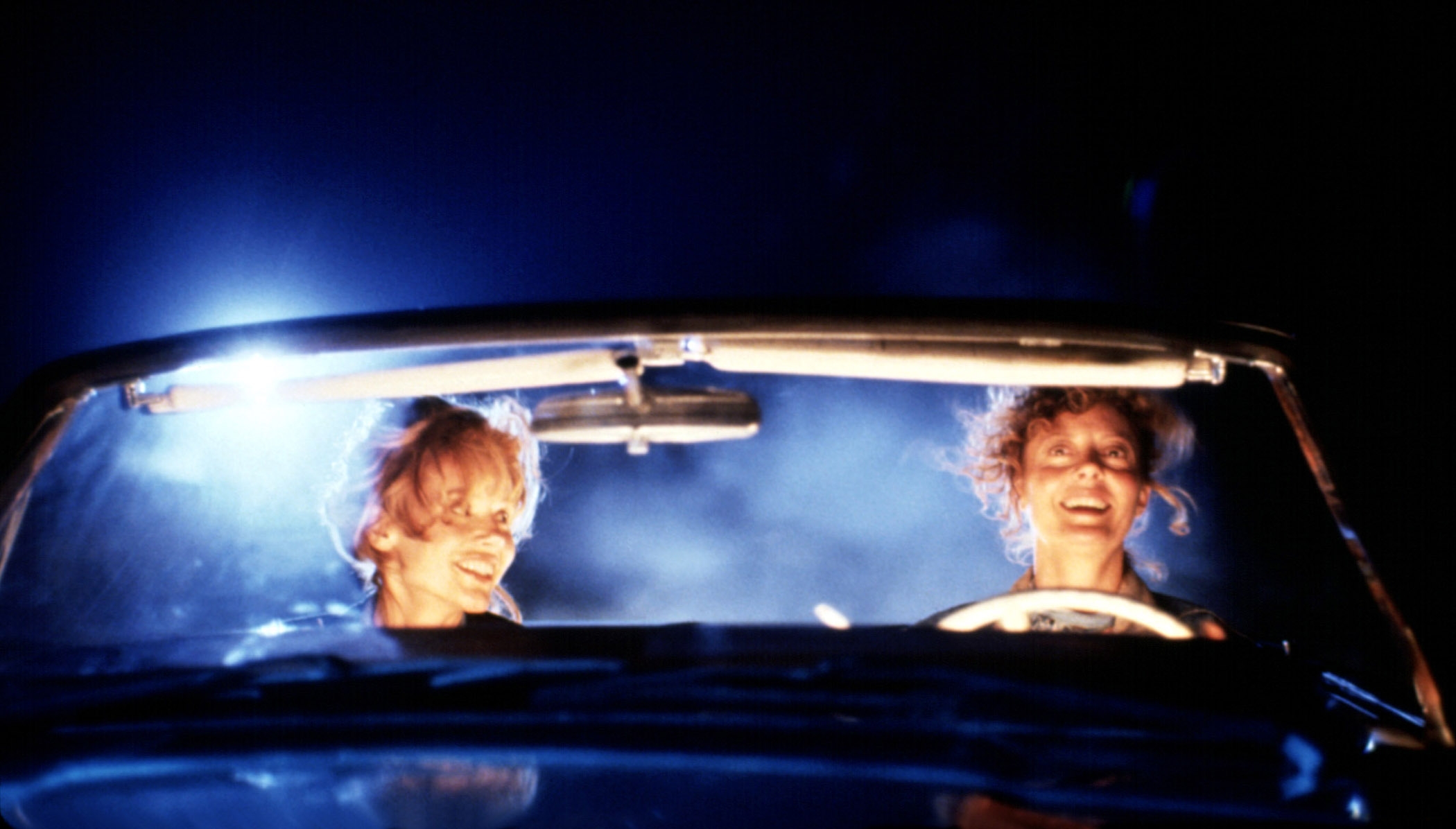 Two people in a convertible car at night, both smiling
