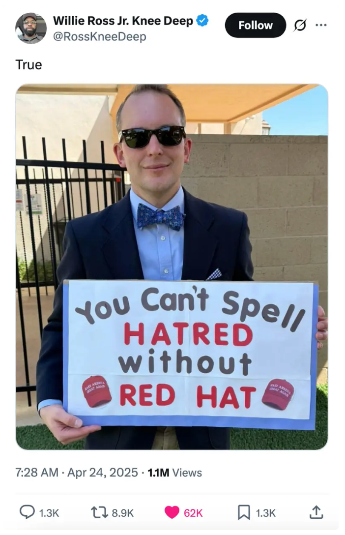 A person in a suit and bow tie holds a sign that reads, &quot;You Can't Spell HATRED without RED HAT,&quot; with red hats illustrated on the sign
