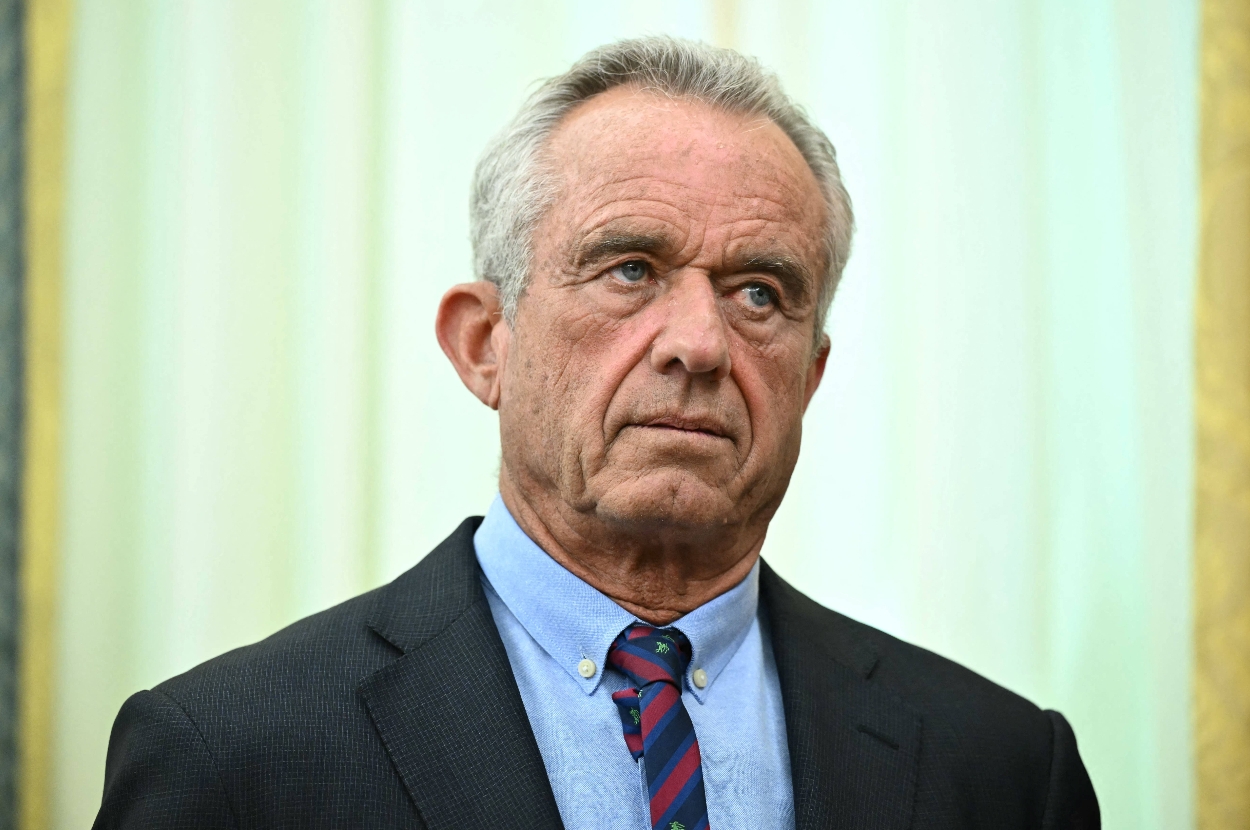 A person in a suit with a striped tie looks serious, standing indoors against a neutral backdrop