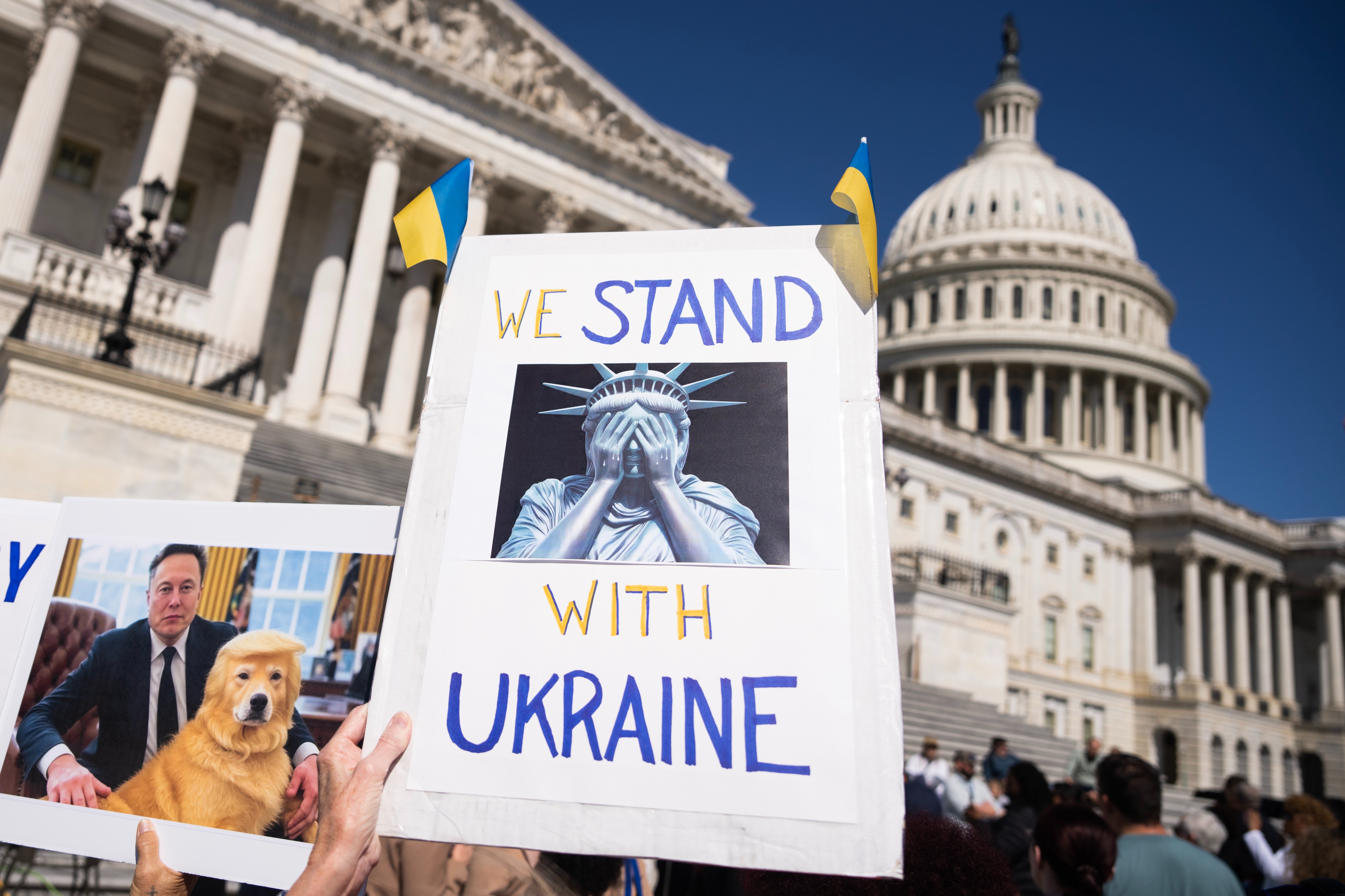 Protesters outside a Capitol building hold signs supporting Ukraine, one featuring the Statue of Liberty with her face in her hands