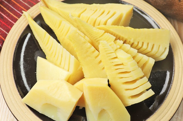 木製テーブル上の皿に、ゆでたタケノコのスライスが盛られている。