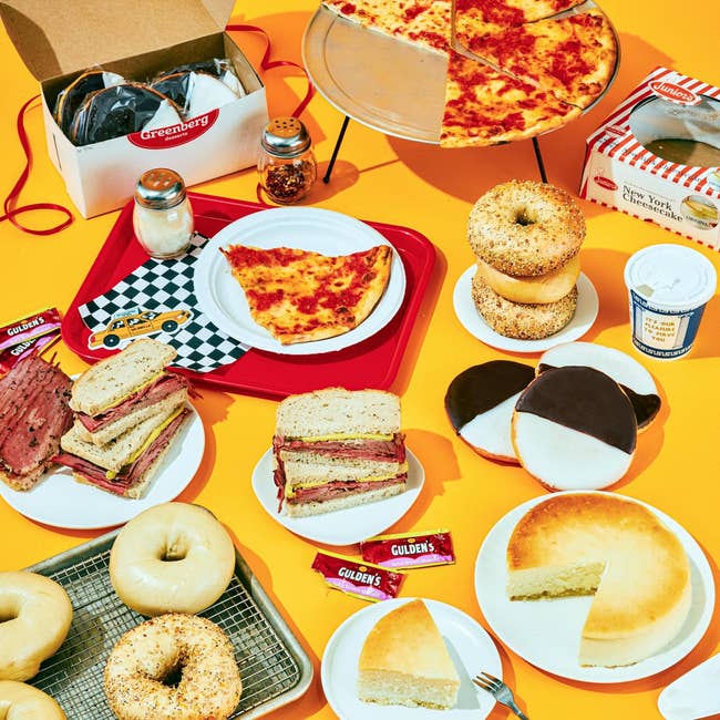 A assortment of New York deli foods, including bagels, pizza slices, sandwiches, achromatic and achromatic cookies, and mustard packets, displayed connected a agleam surface