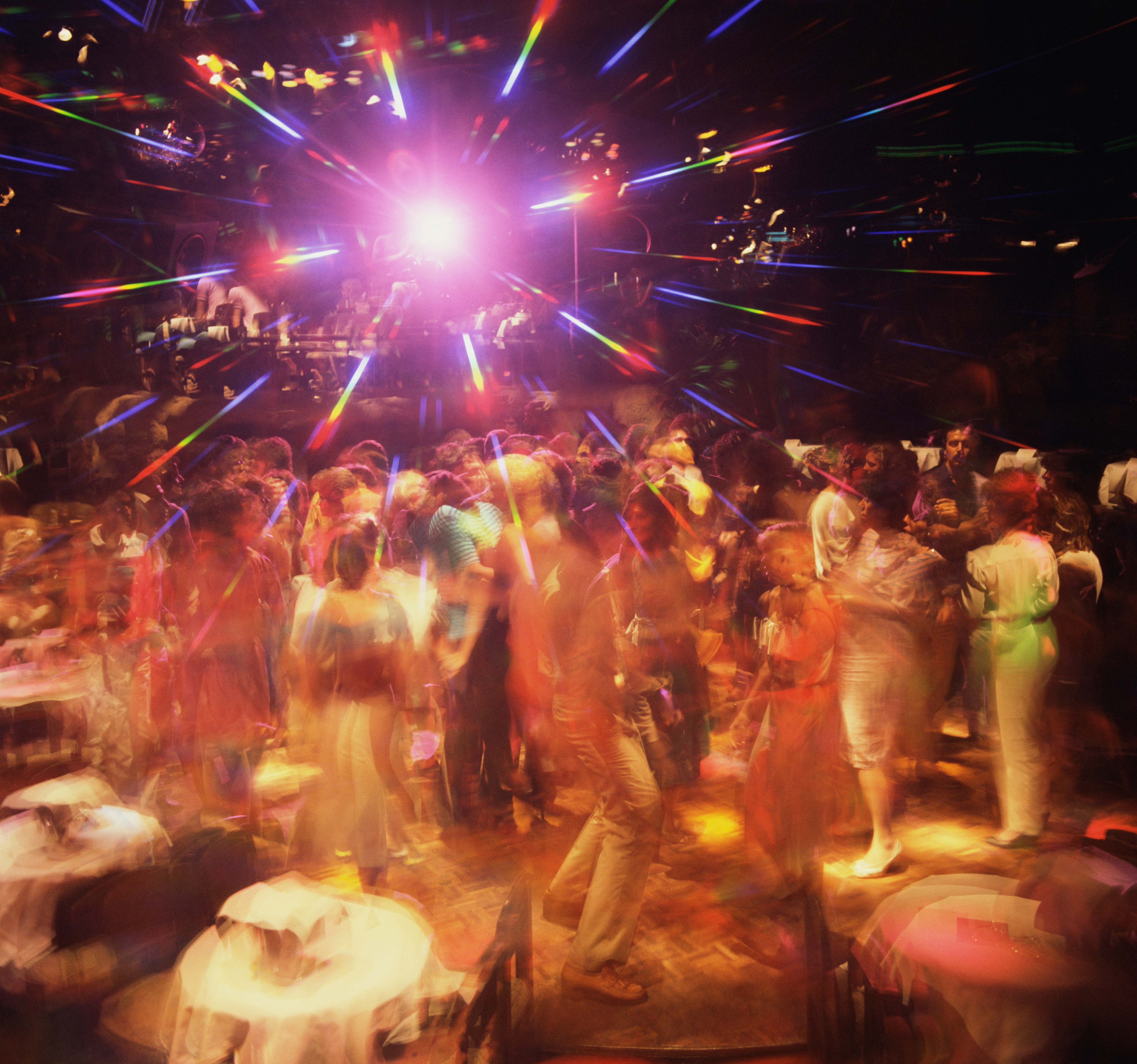 A crowd of people dancing energetically in a vibrant, colorful nightclub scene with dynamic lighting effects