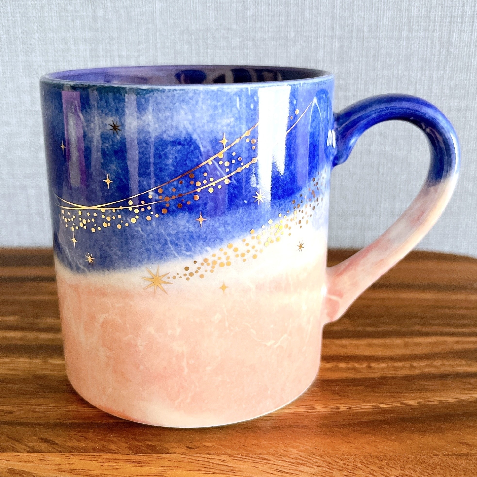 星とラインが描かれたグラデーションのマグカップ。木のテーブルに置かれている。